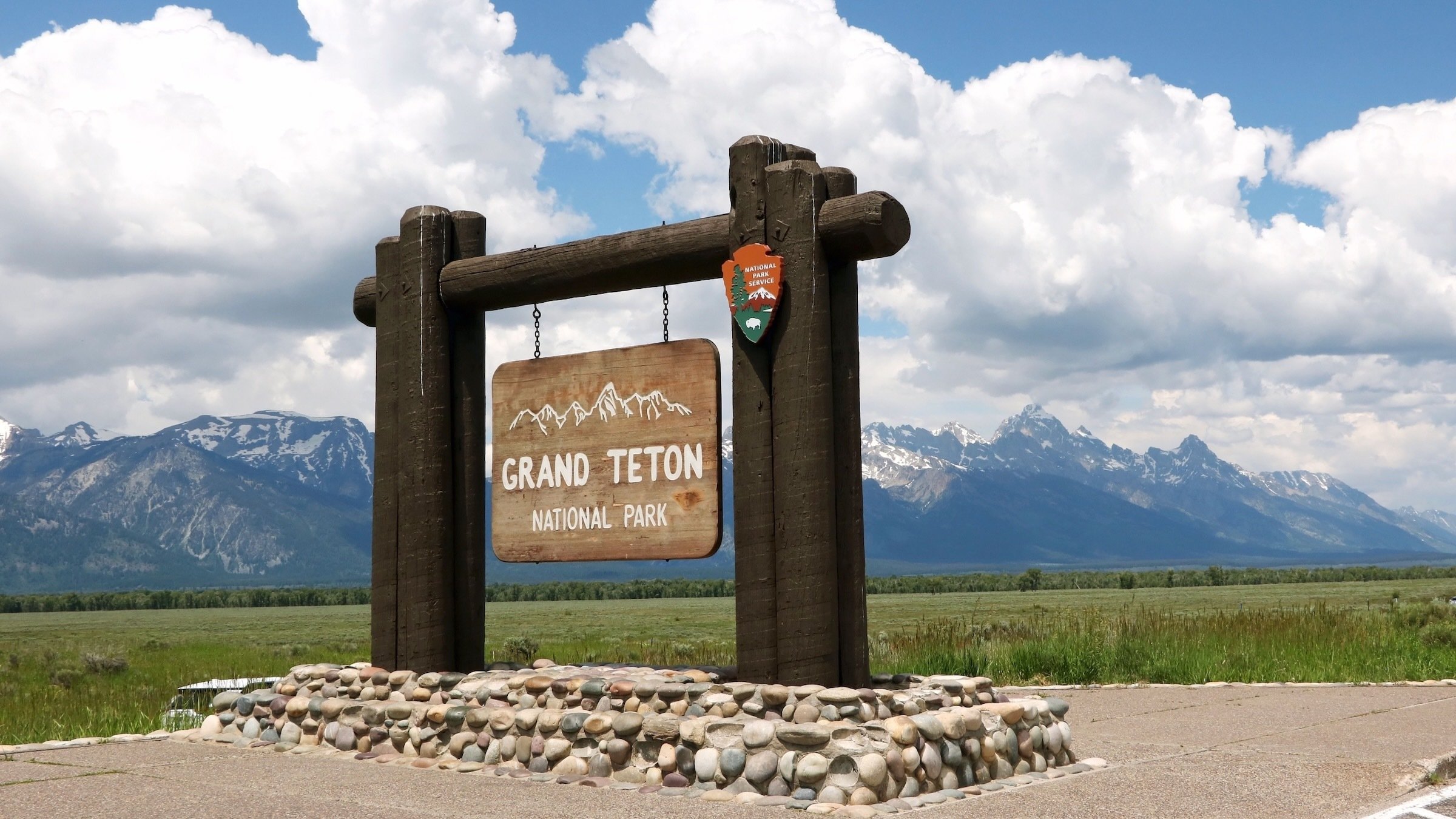 A wooden sign for Grand Teton National Park against a stunning backdrop of mountains and clouds.