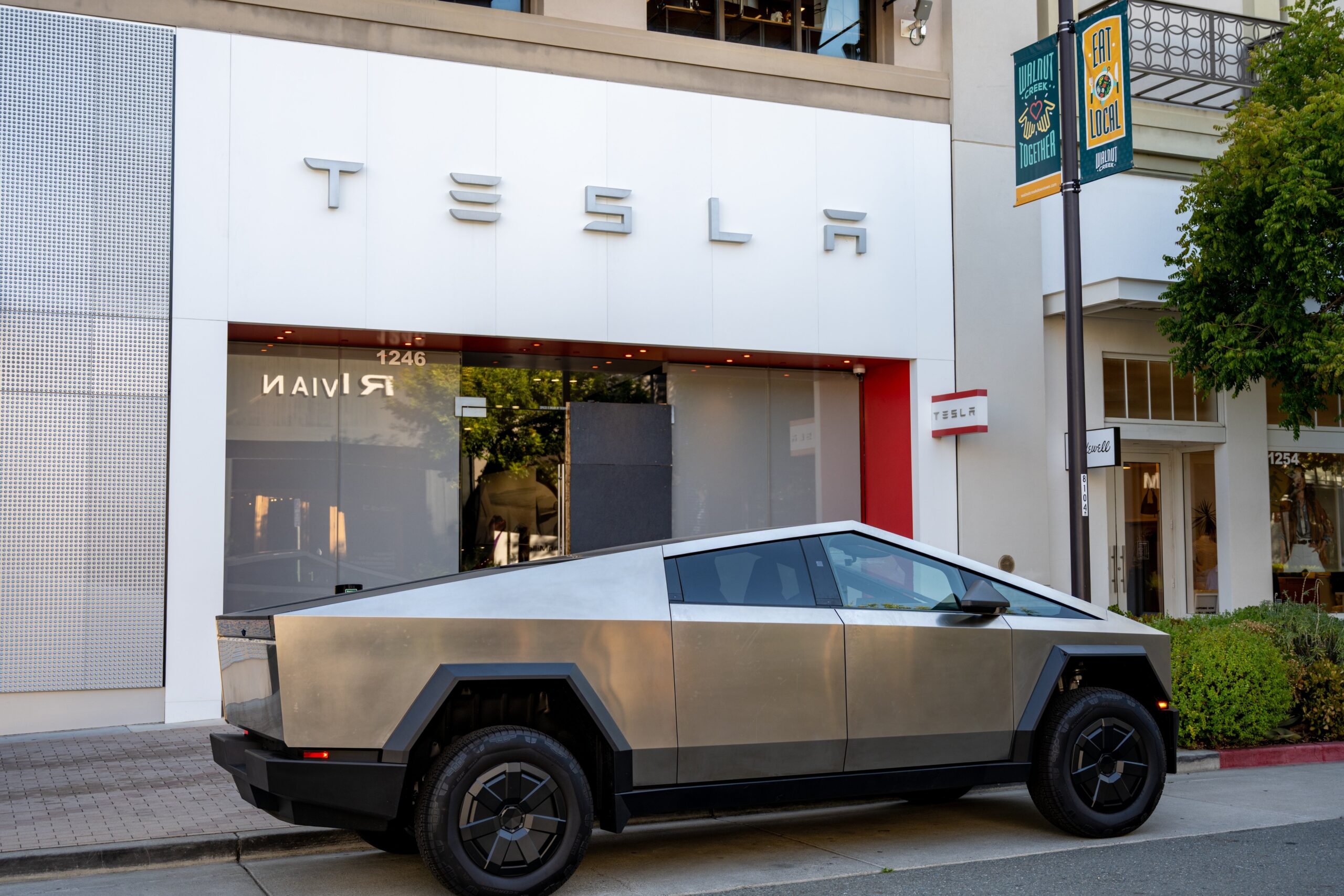 Tesla Cybertruck is parked outside a Tesla store with signage and logos visible