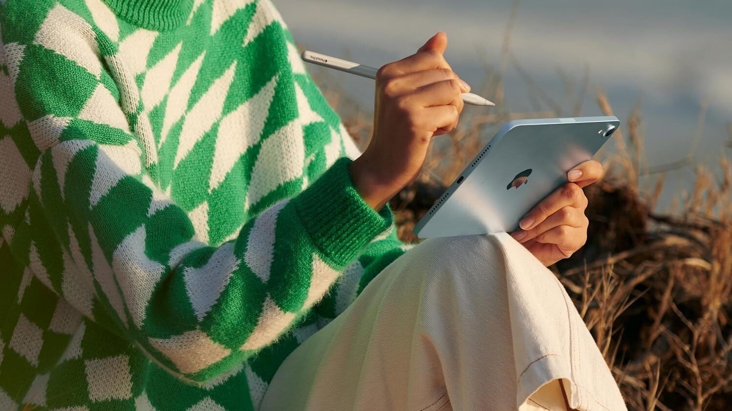a person sits outside, writing on the apple ipad mini with the apple pencil