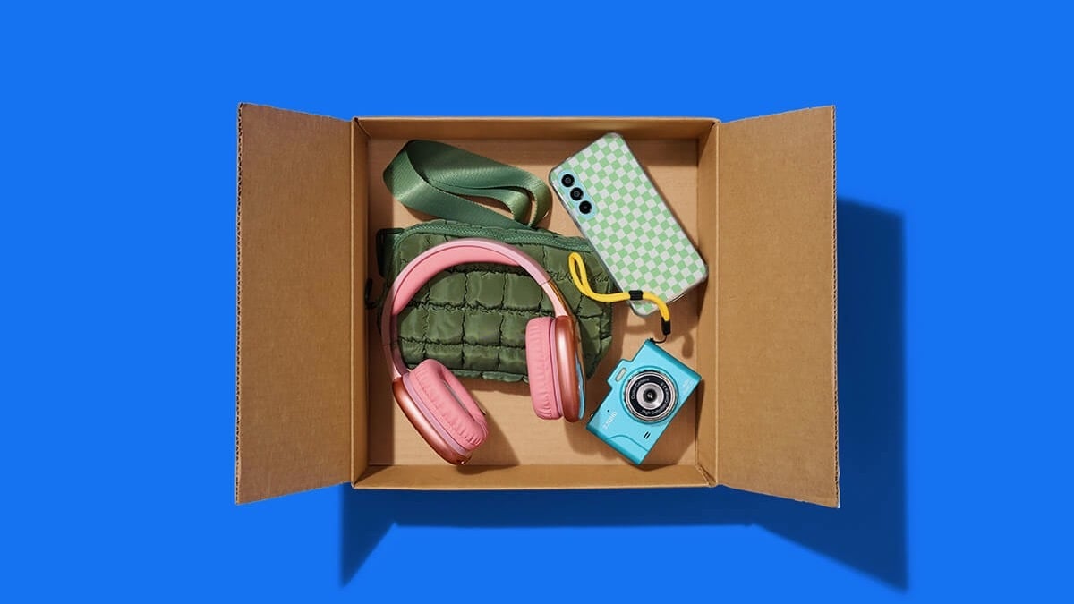 open amazon prime shipping box filled with headphones, smartphone, camera, and clutch bag