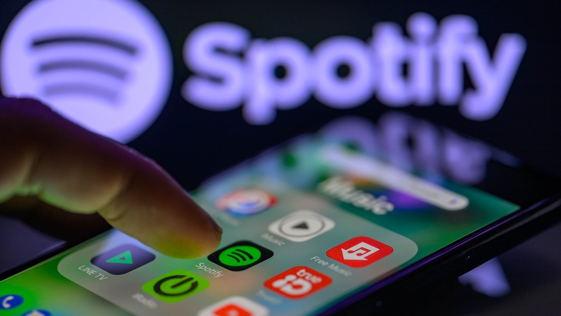 The Spotify app icon is being displayed on a smartphone with Spotify visible in the background.