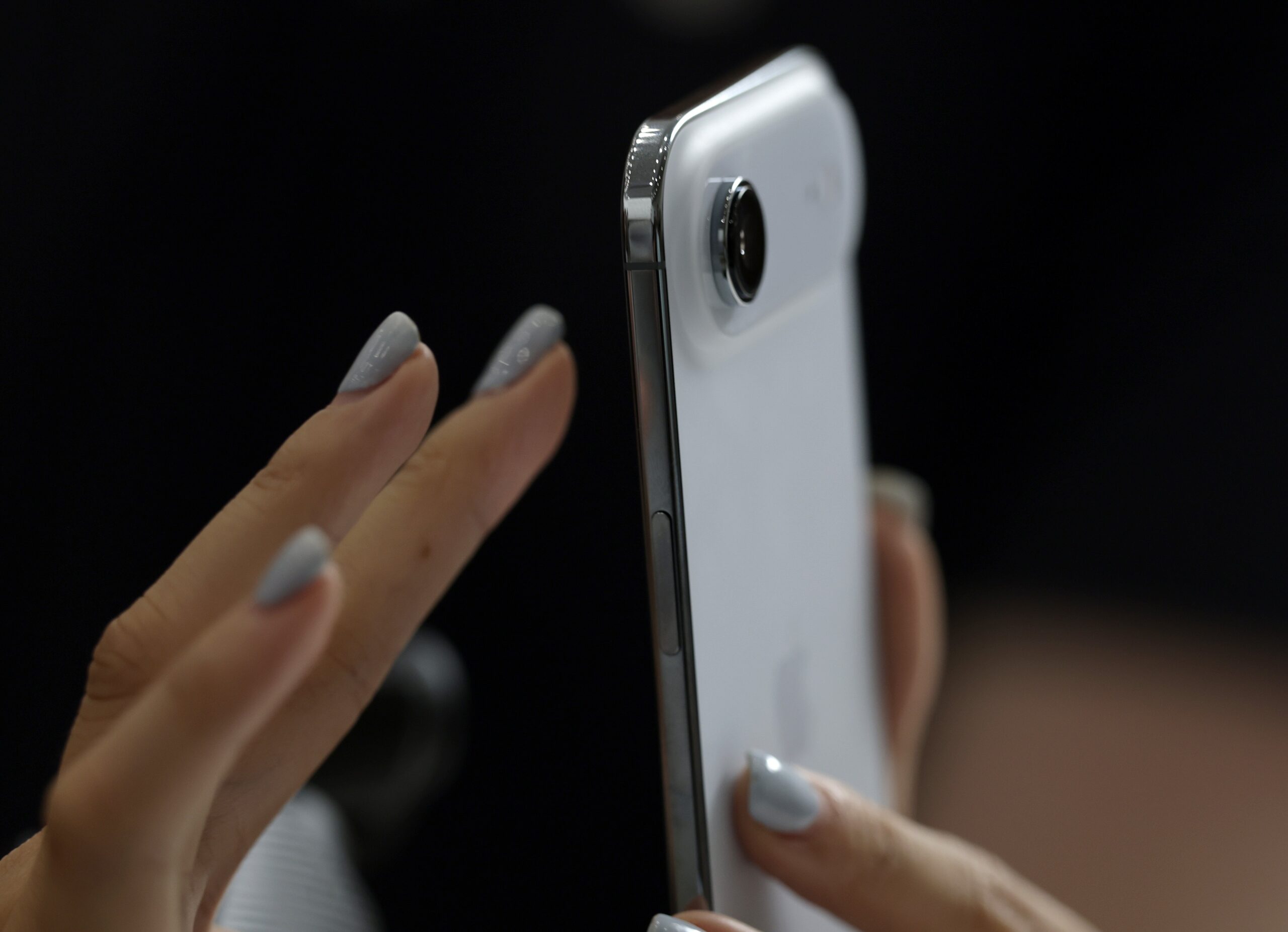 A hand with painted nails taps on the screen of a new iPhone Air.