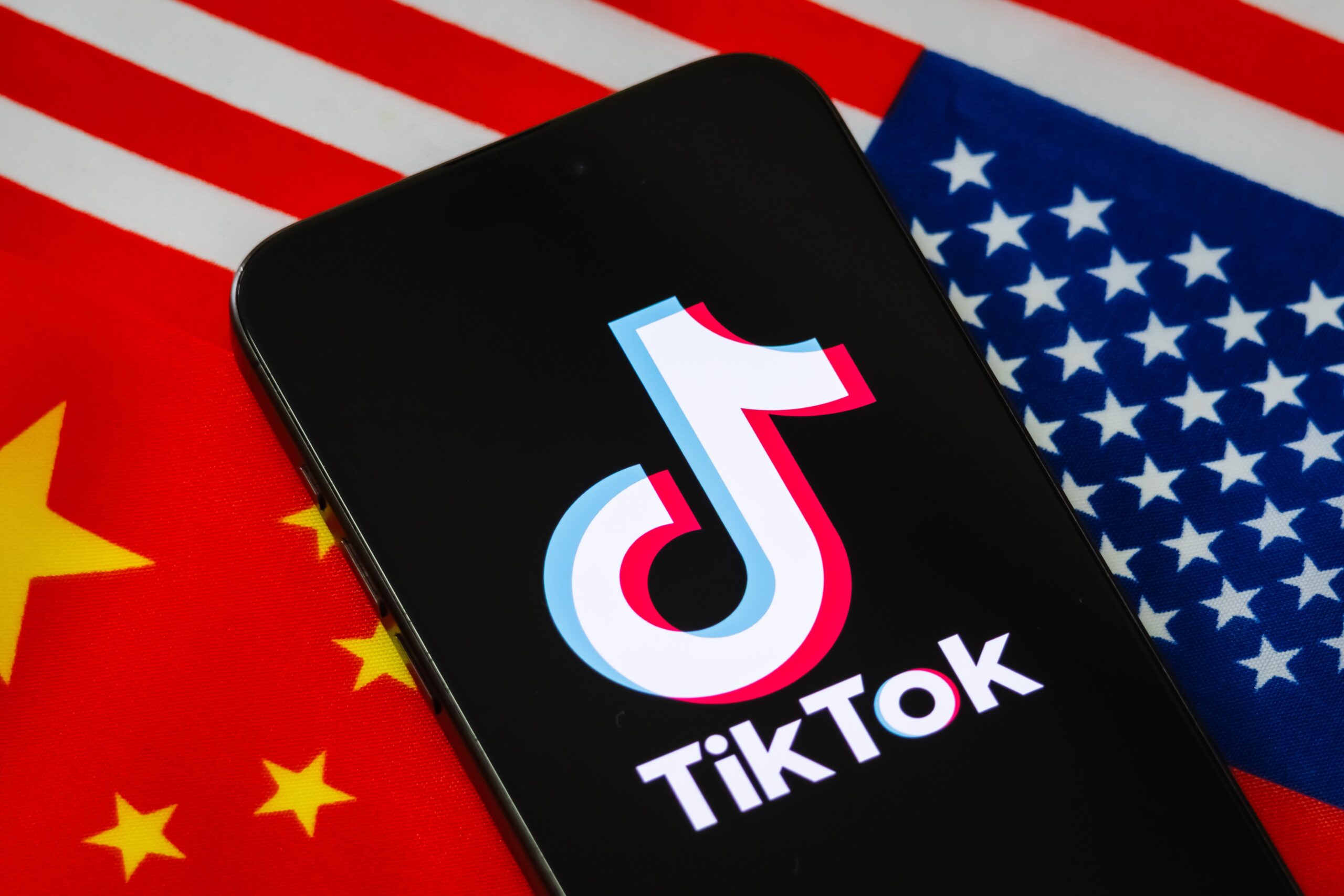 a tiktok logo on a phone with the american and chinese flags behind it