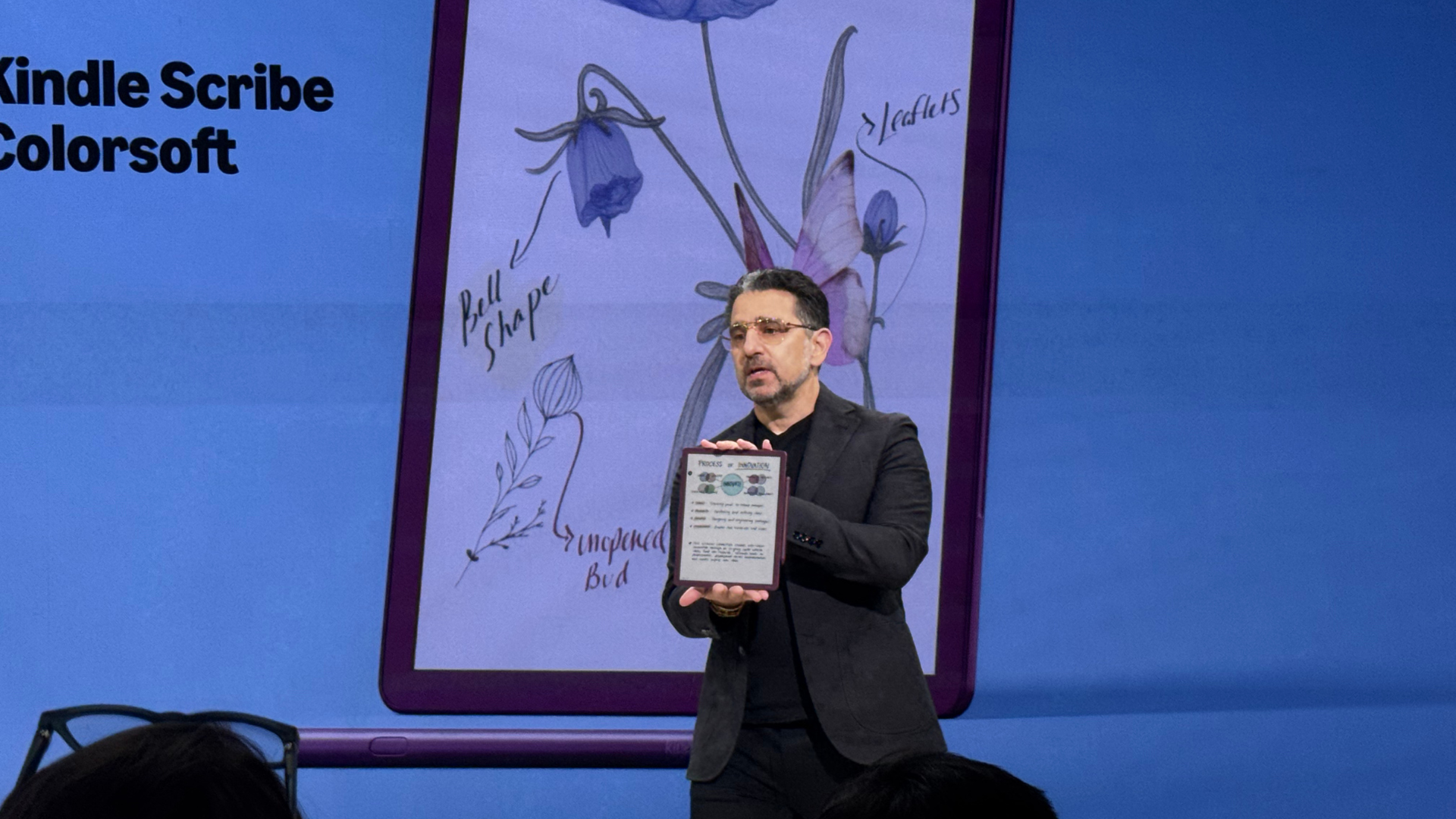 A person holding up a Kindle Scribe Colorsoft on a stage.