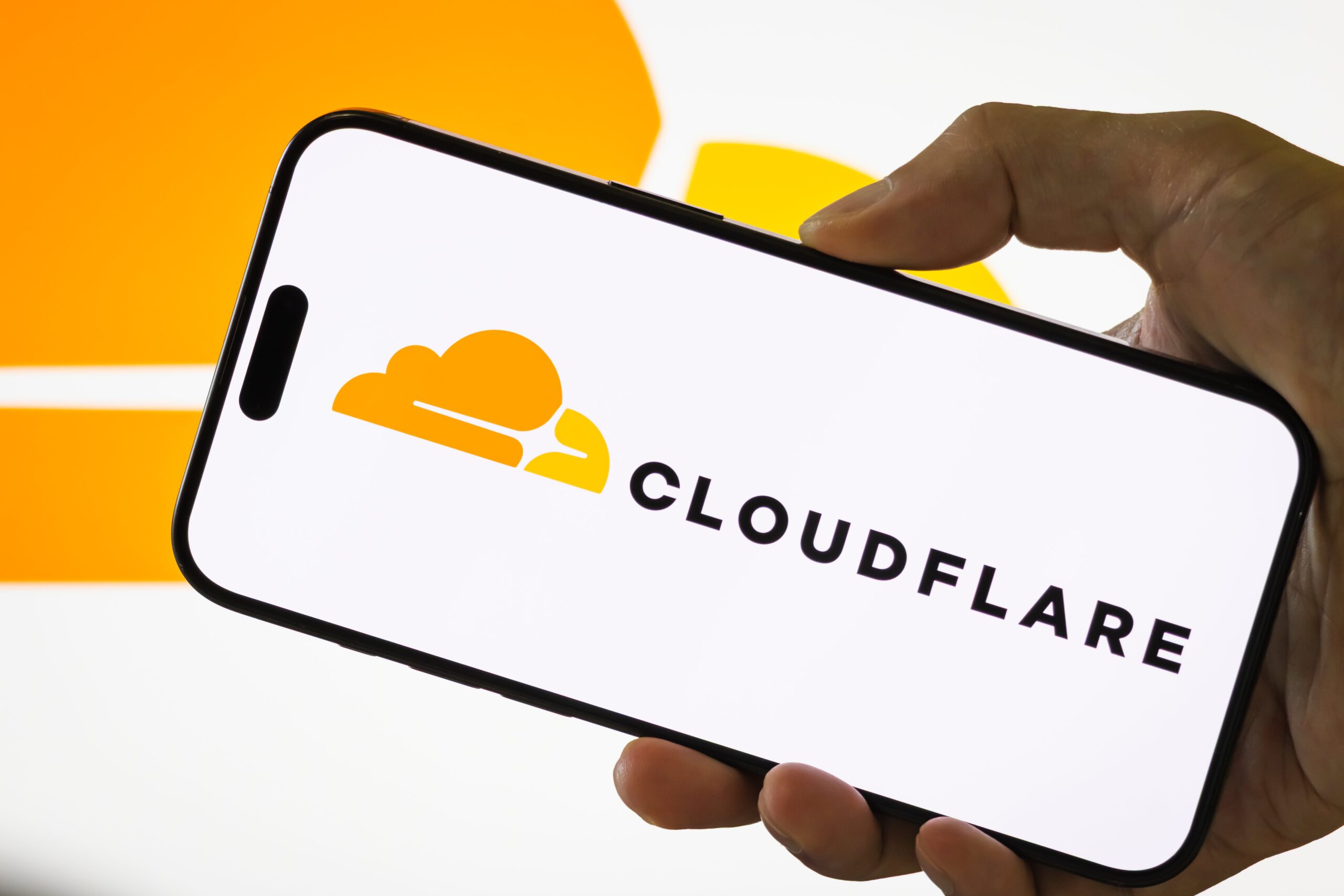 A person holds a smartphone displaying the logo of Cloudflare Inc. (NYSE: NET), an American web infrastructure and website security company, with the company's cloud logo visible in the background, on July 29, 2025 in Chongqing, China.