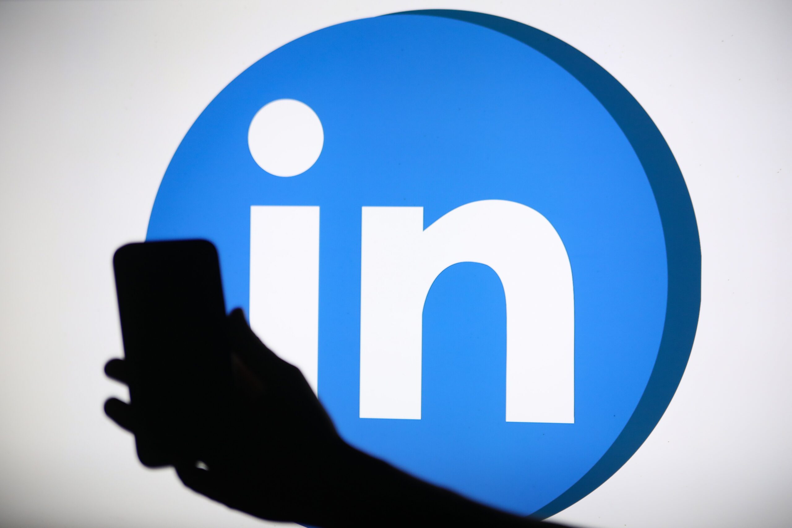 The LinkedIn logo displays on a screen with a person holding a phone