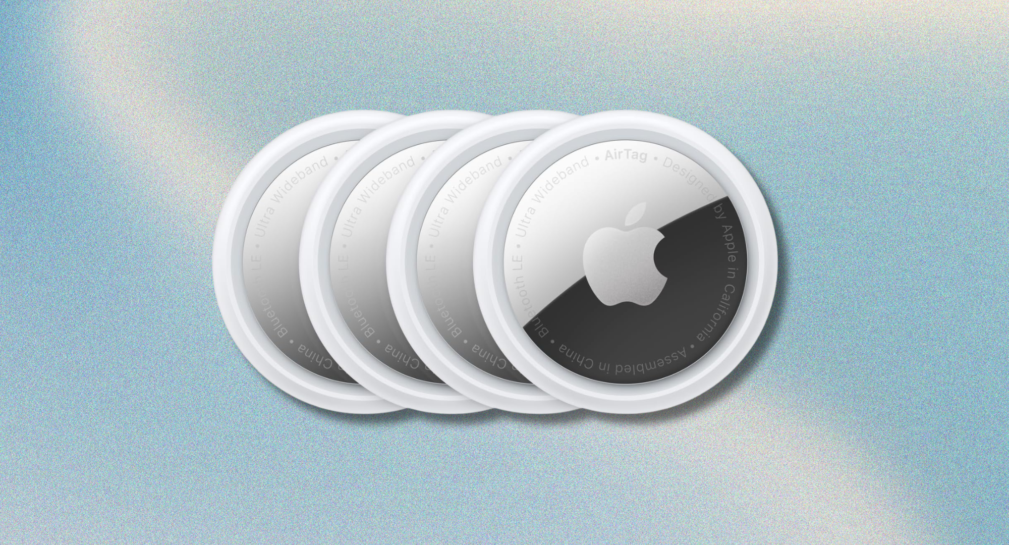 Four Apple AirTags against a blue, grainy background.