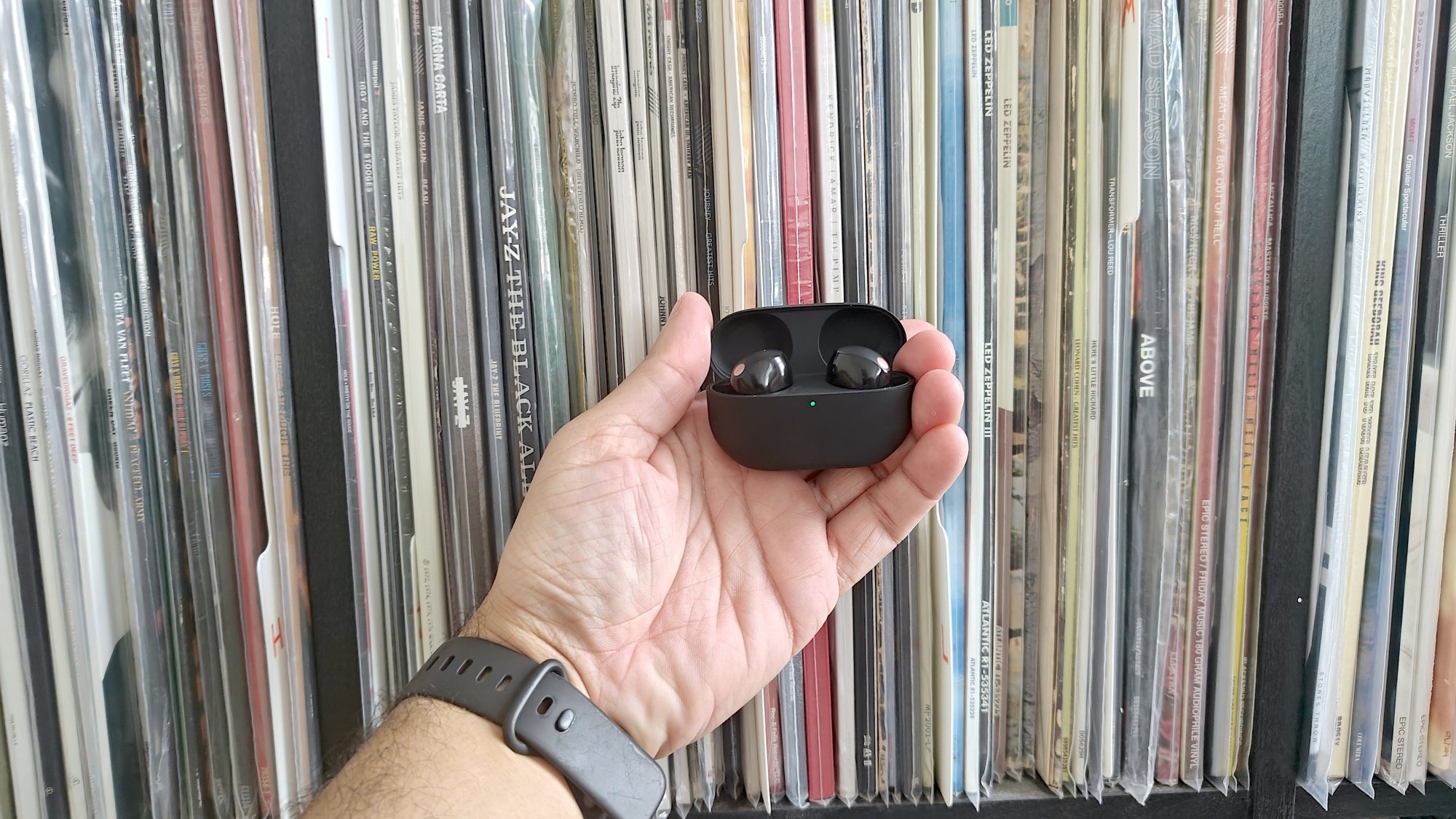 person's hand holding sony earbuds against records on a shelf