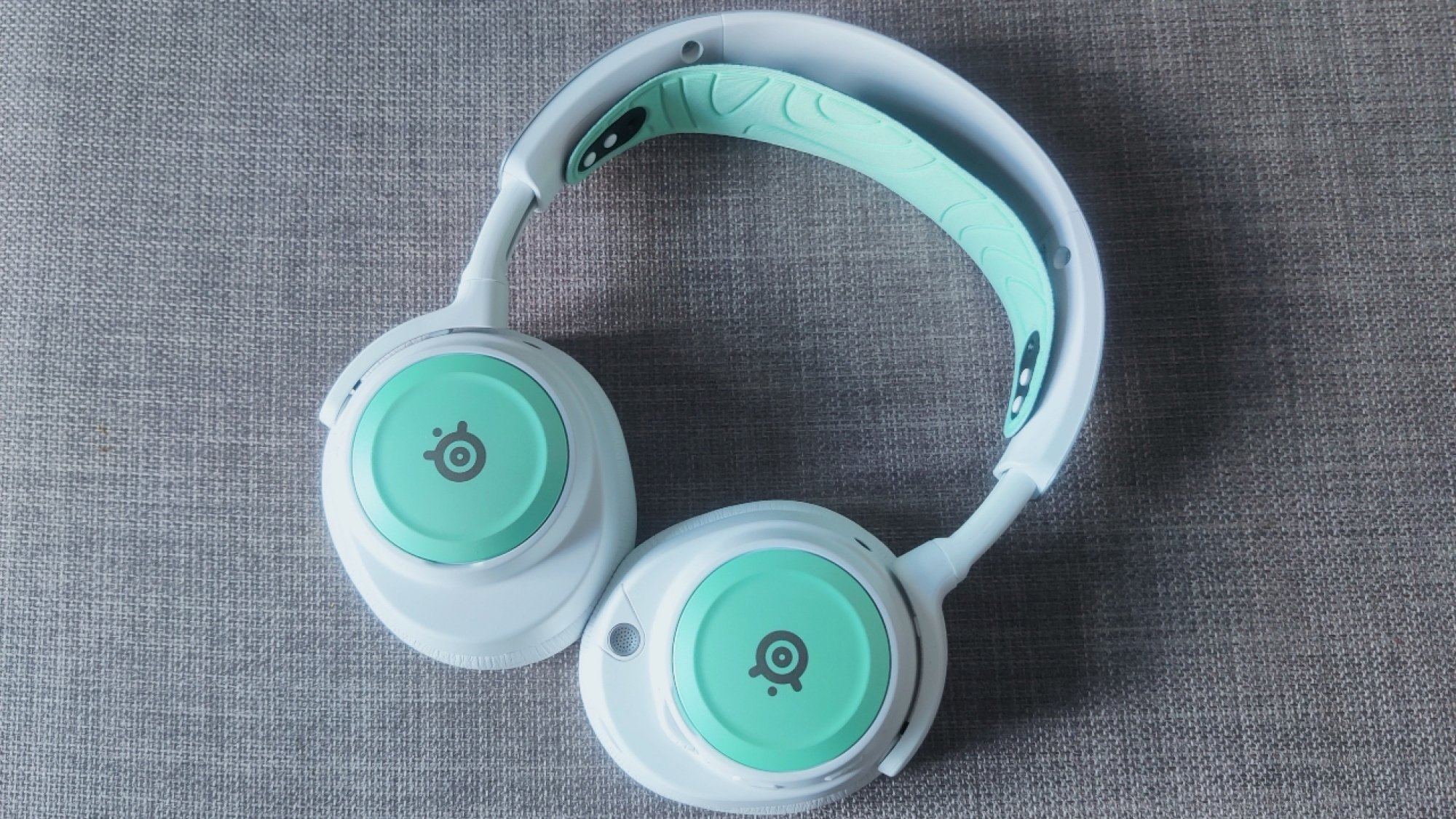 The SteelSeries Arctis Nova Pro Wireless in white with mint speaker plates and headband, with its earcups swivelled round