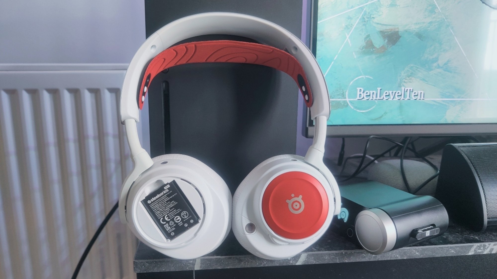 The SteelSeries Arctis Nova Pro Wireless with red cherry speaker plates & headband, with one removed showing the swappable batteries