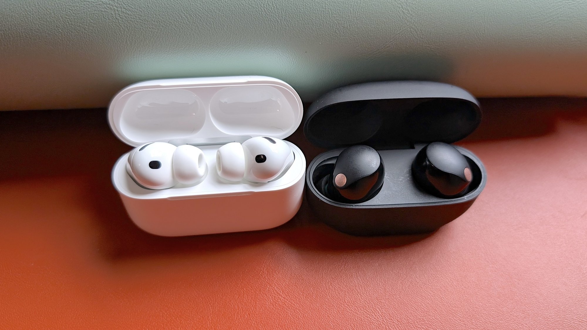 The white Apple AirPods 3 sitting in their case next to the black Sony WF-1000xM5 earbuds in their case