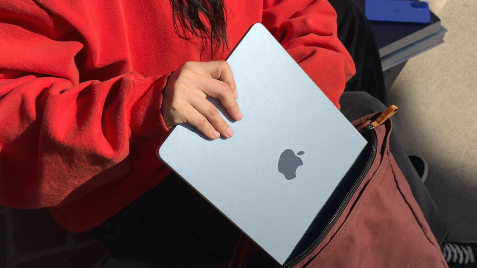 person sliding sky blue MacBook Air into backpack