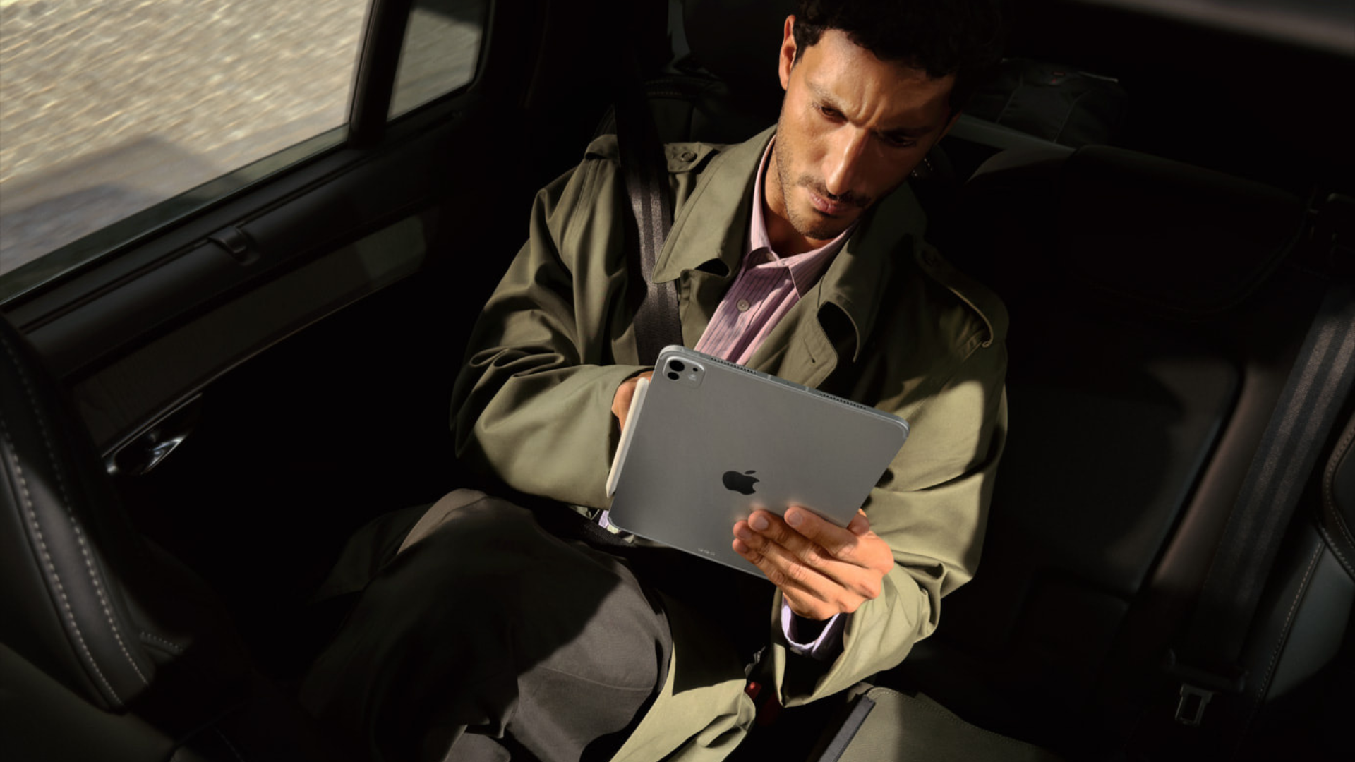 A man in the back of a car holding up an iPad Pro