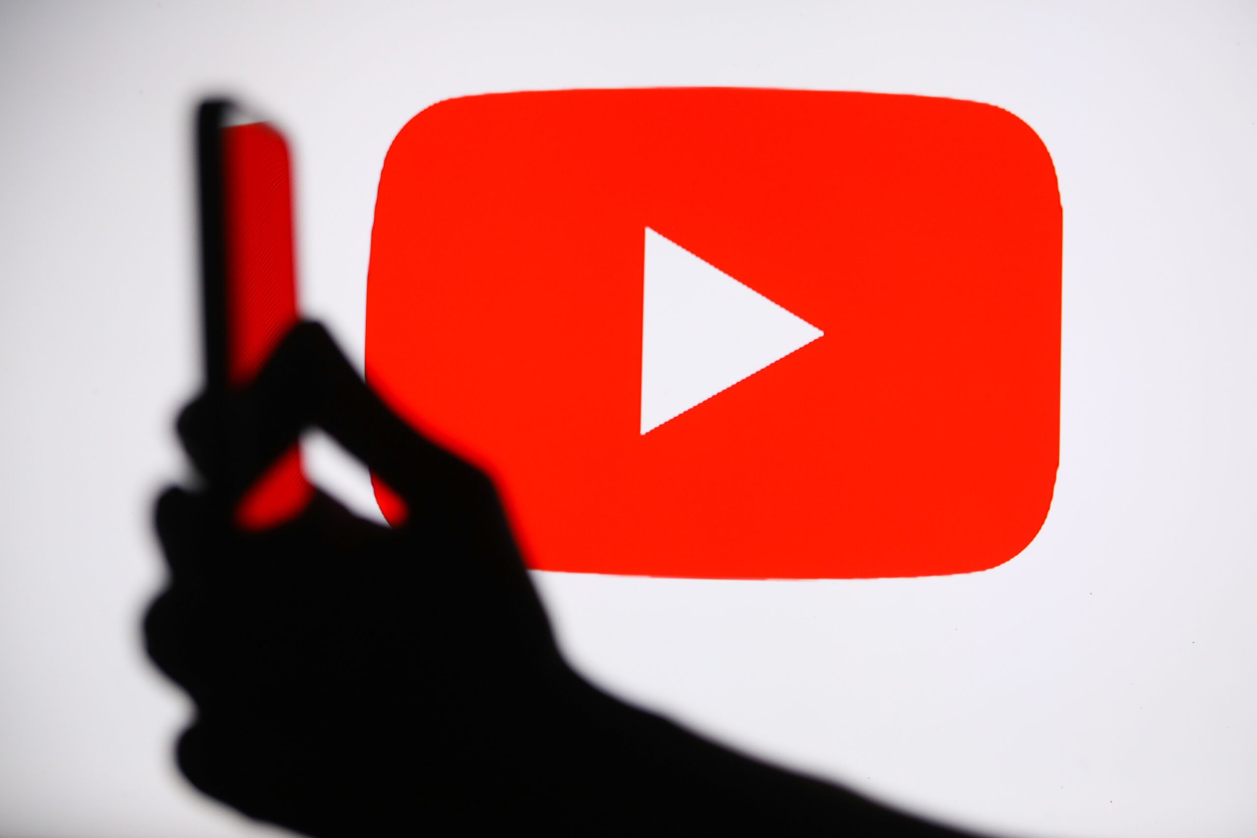 An image of the YouTube logo with a hand holding a smartphone in the foreground.