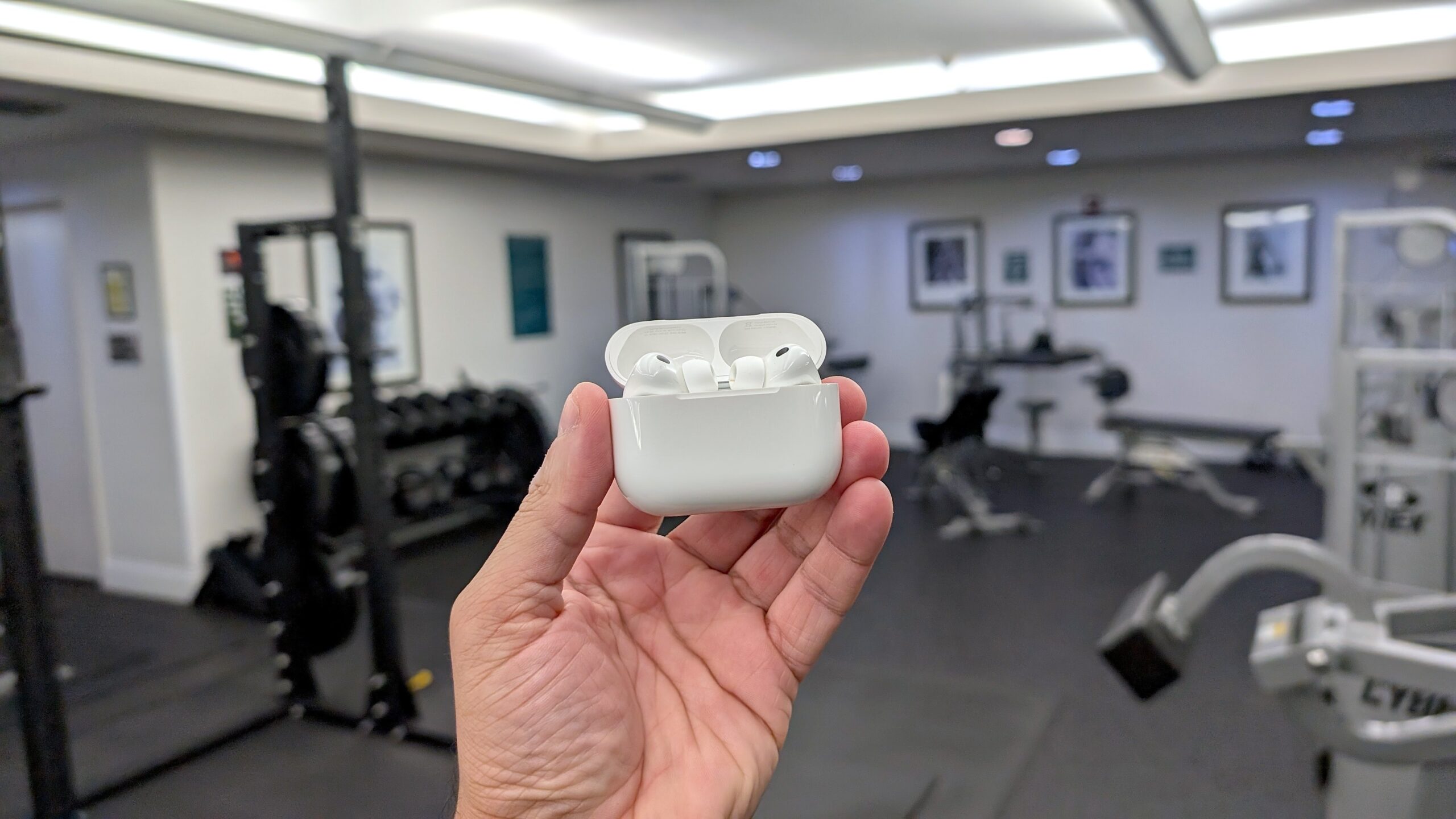 person holding airpods pr case in front of gym equipment