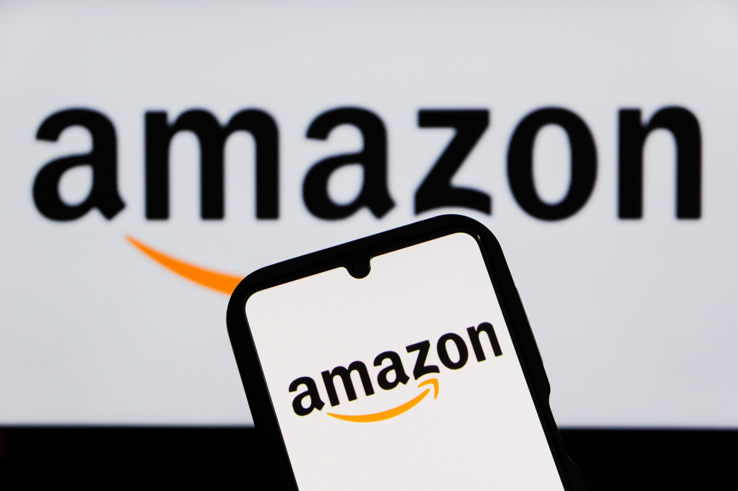 A smartphone shows the Amazon logo, with a larger Amazon logo visible in the background.