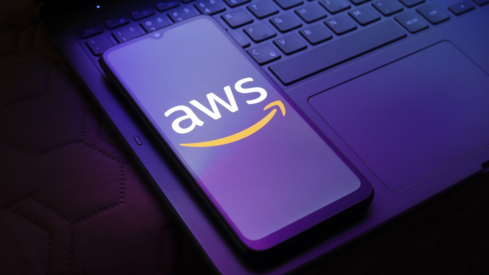 AWS logo on a smartphpne resting on a laptop under purple light.