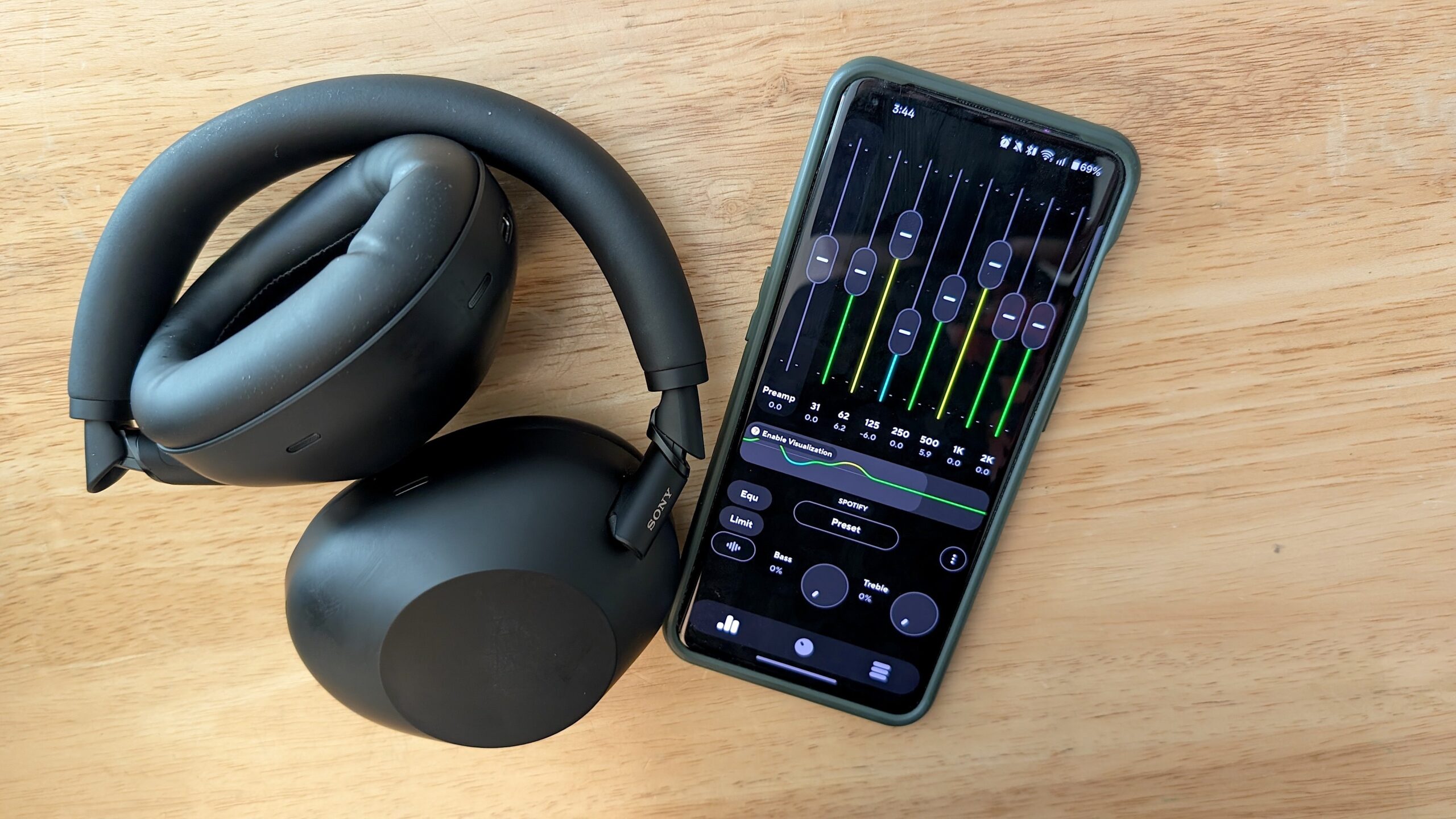 A pair of headphones resting on a table next to a phone with EQ settings open on the screen.