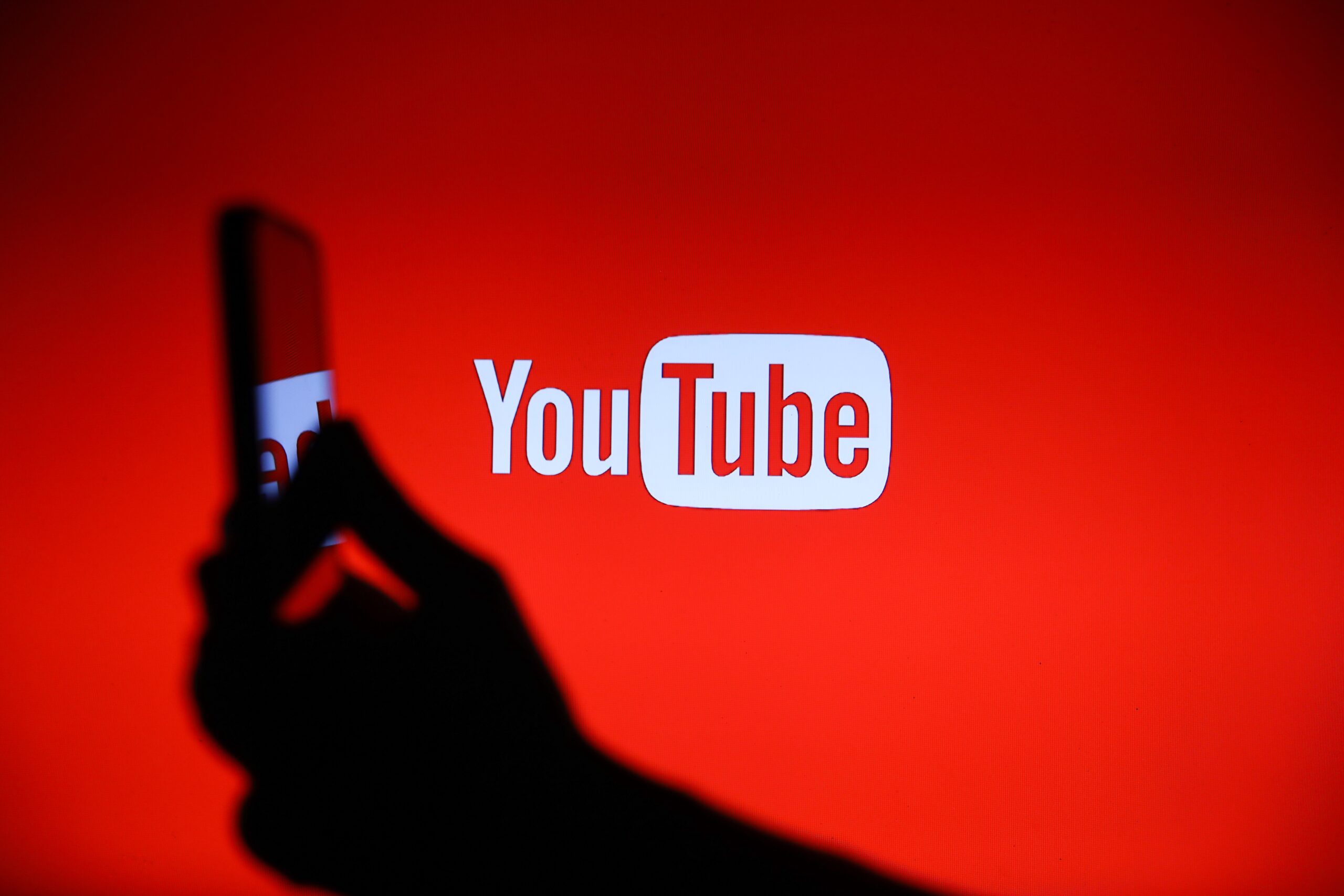 The YouTube logo displays on a screen with a person holding a phone.