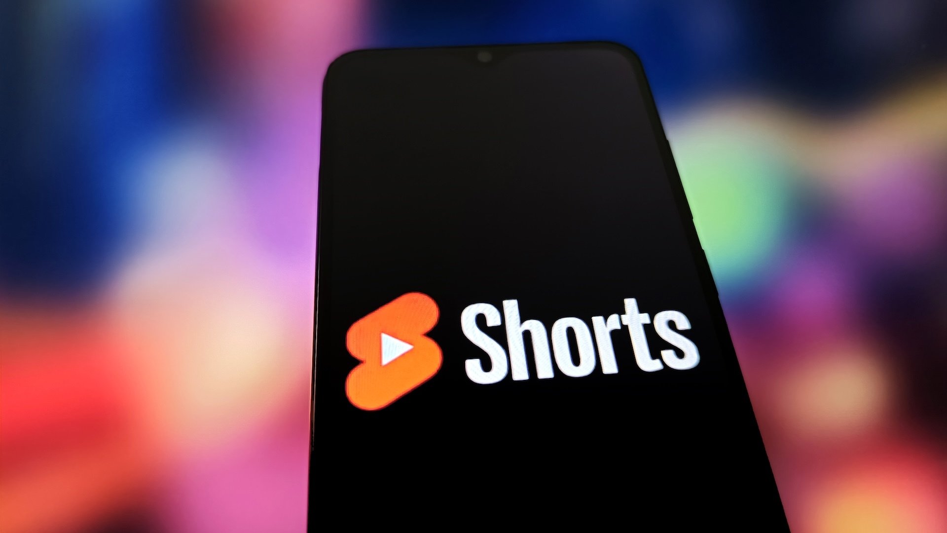 YouTube Shorts logo on a smartphone in front of a colourful background.