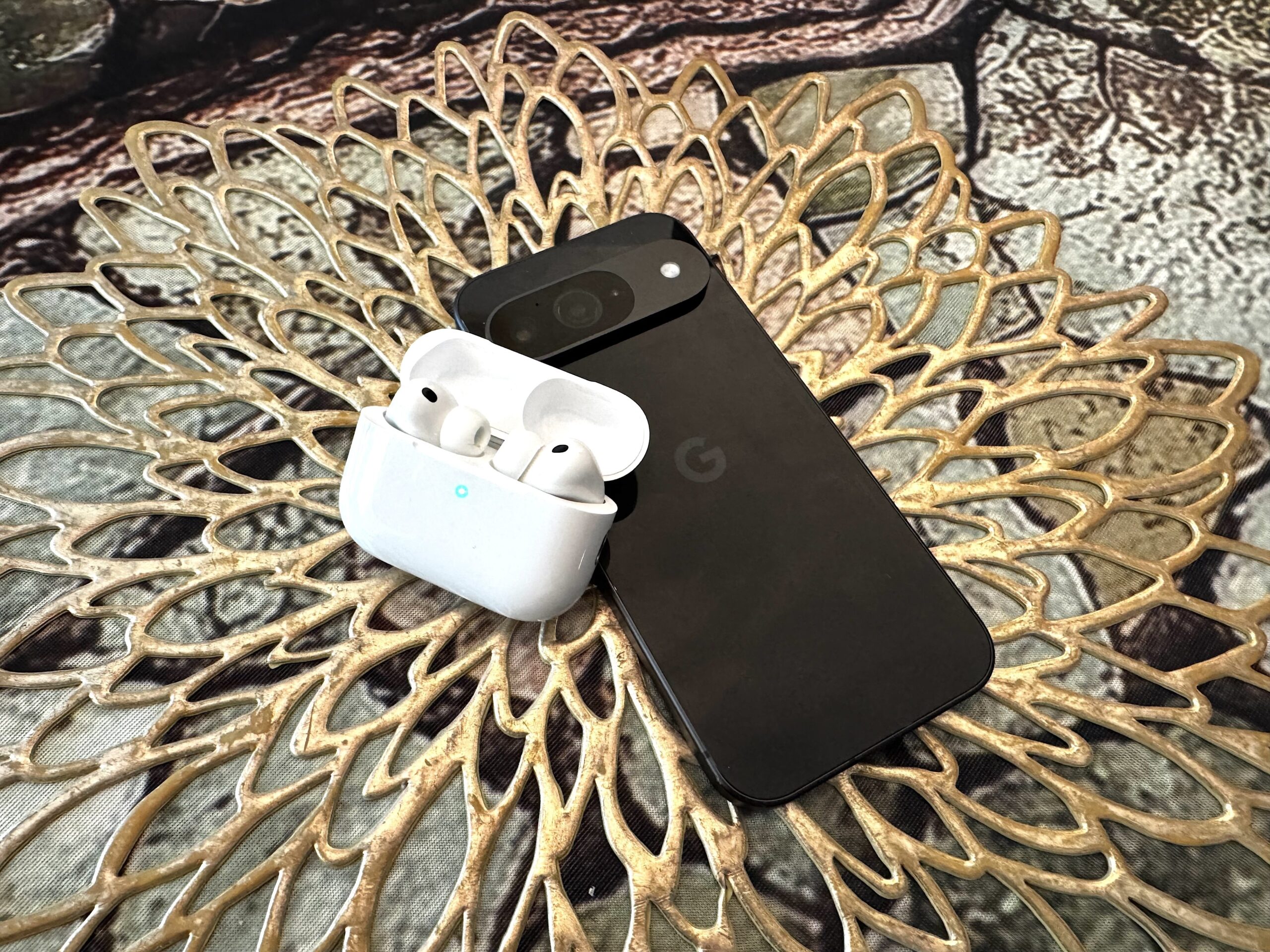 Apple's AirPods Pro 3 in their case, sitting on a table next to a Google phone