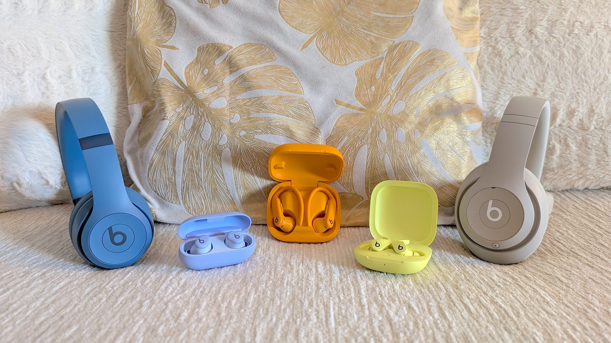 The Beats Studio Pro, Beats Fit Pro, Beats Solo 4, Beats Solo Buds, and Beats Powerbeats Pro 2 next to each other on a sofa.