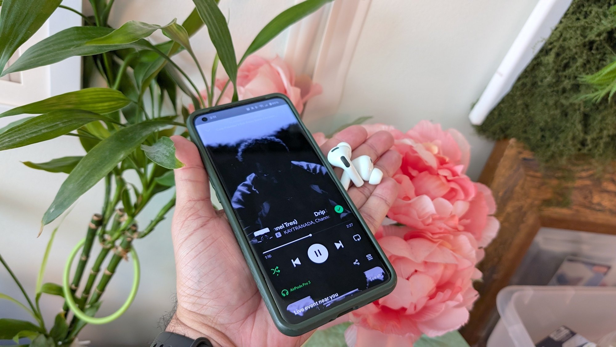 A phone with Spotify open to Kaytranada’s song "Drip Sweat" and some Apple AirPods Pro 3 next to it