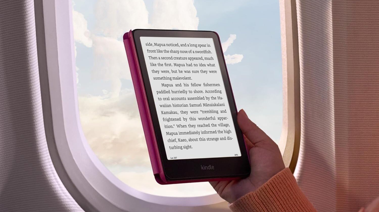 a person holds the amazon kindle paperwhite in front of an airplane window with clouds outside