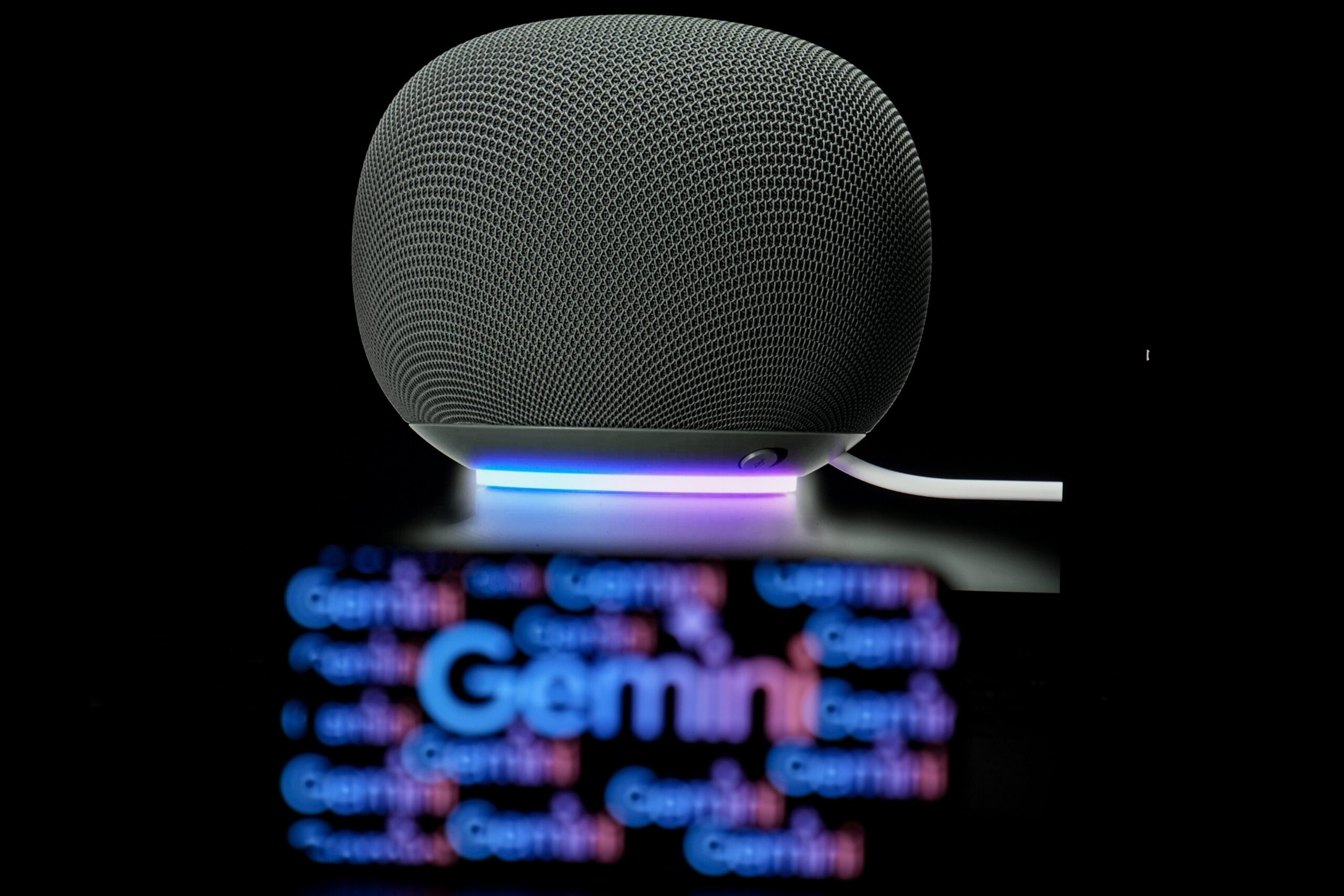  the Gemini logo is displayed on a mobile phone screen in front of a Google smart speaker