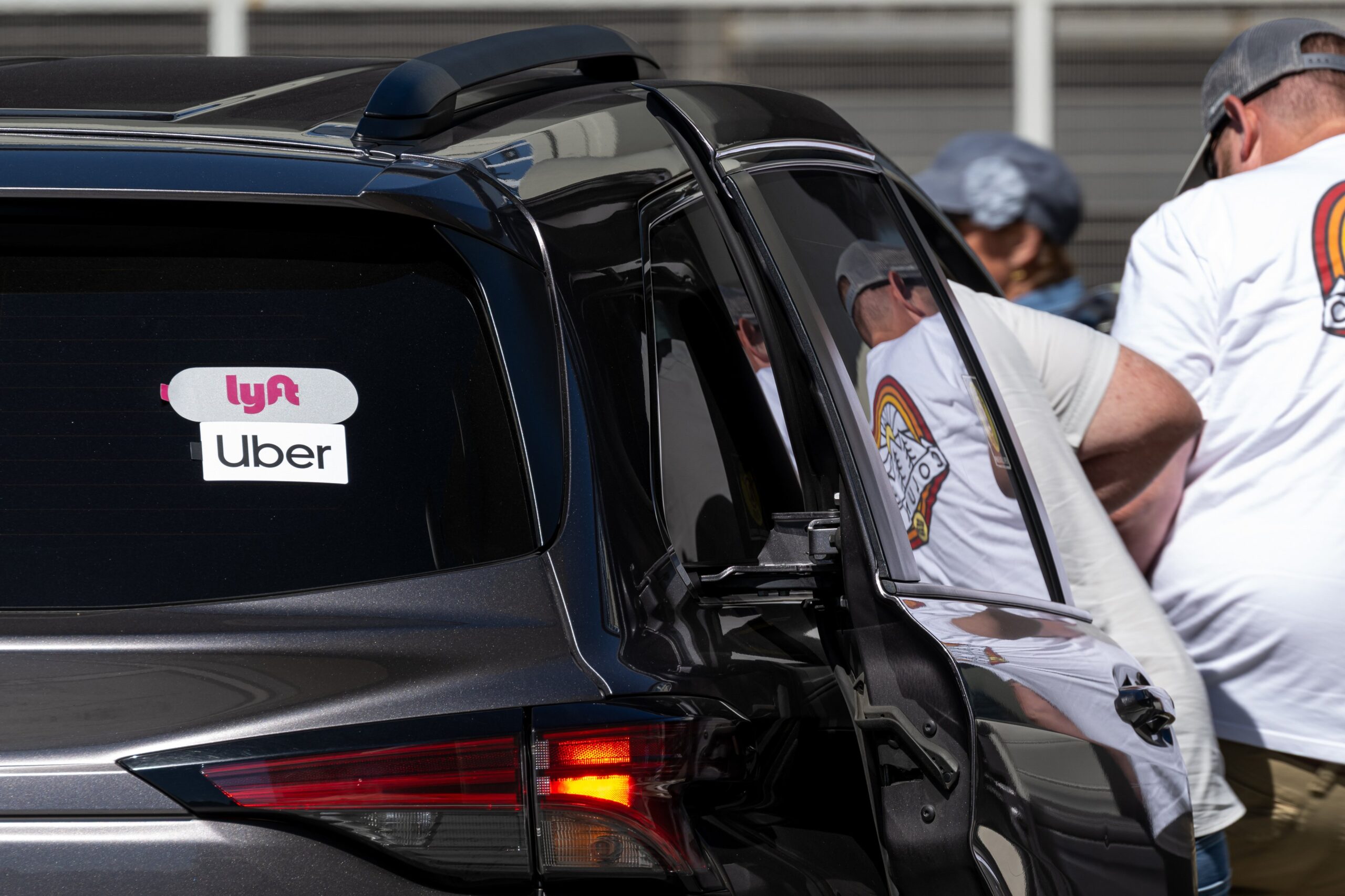 A person gets into the back of a dark car with stickers advertising Uber and Lyft.