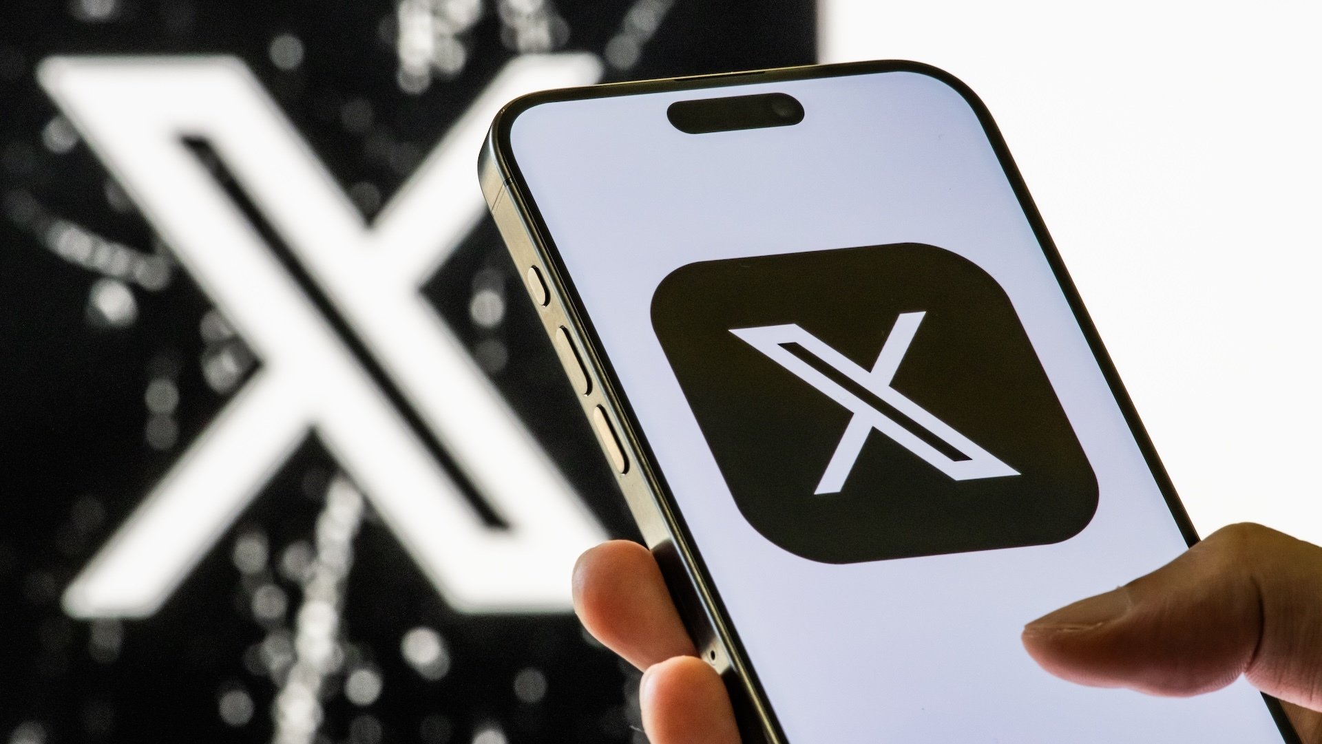 A smartphone shows the app icon for X with a black background, while another X logo is seen in the background.