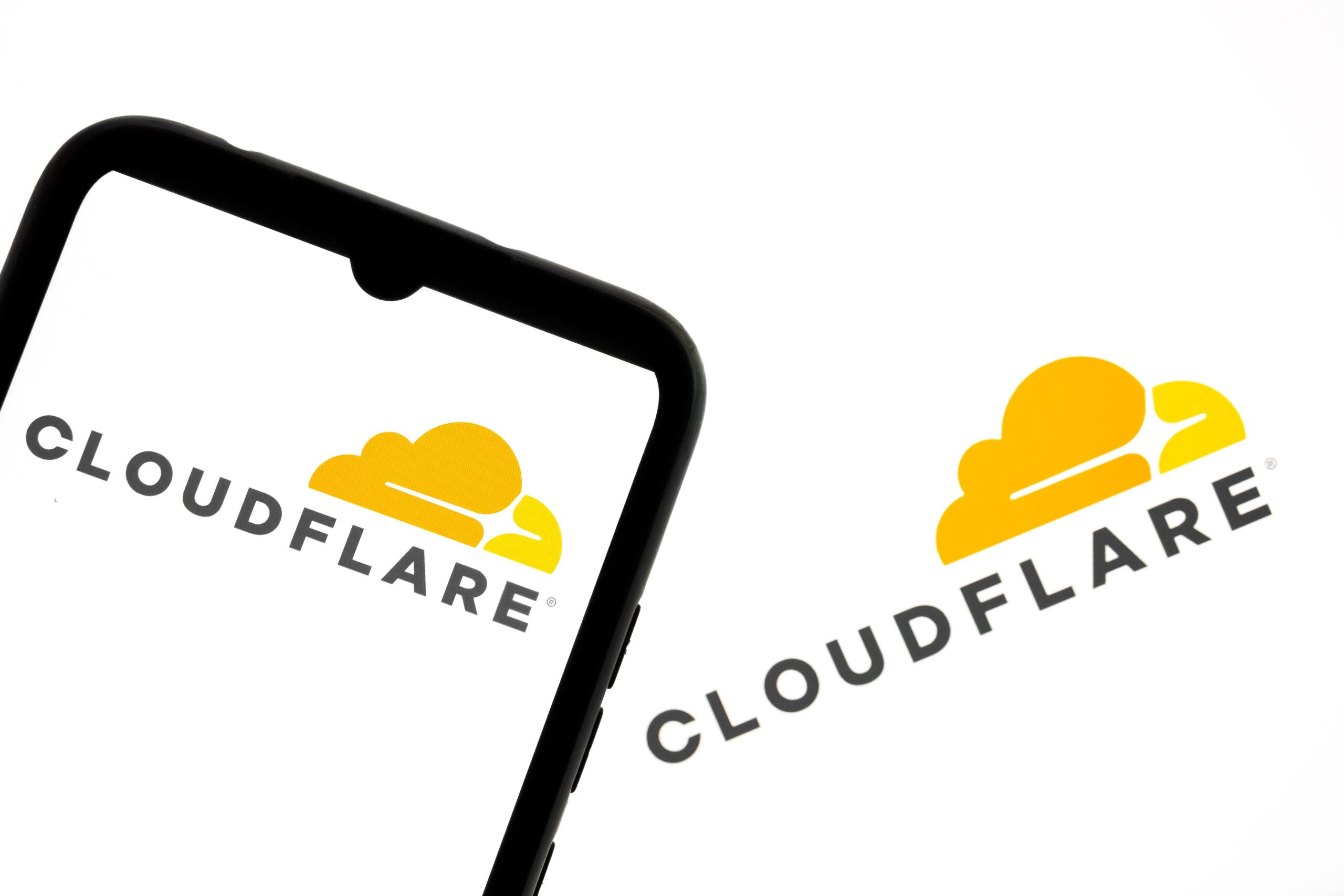 The Cloudflare logo appears on a smartphone screen and as the background on a laptop computer screen