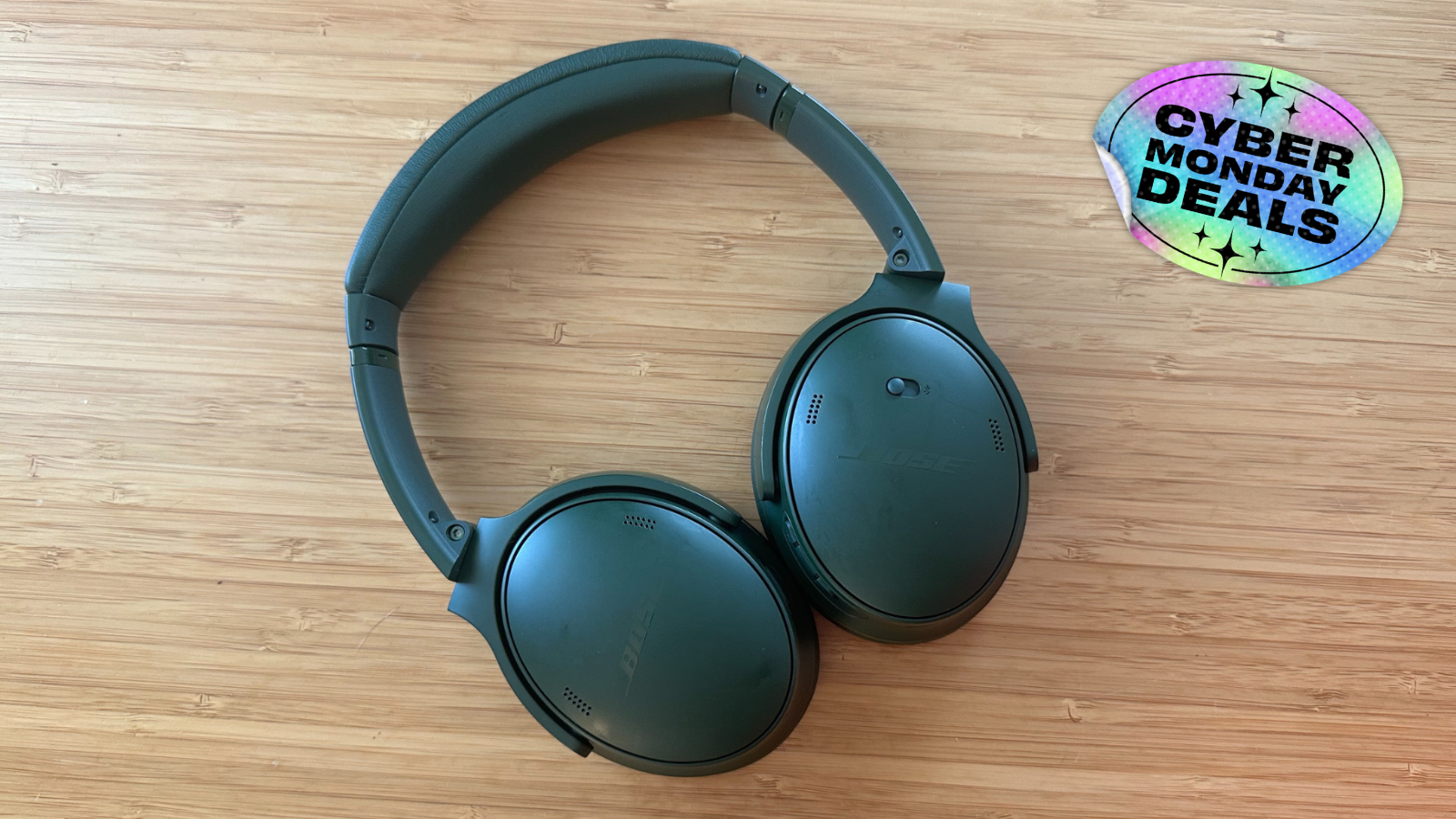 the bose quietcomfort headphones on a wooden surface next to a cyber monday deals sticker