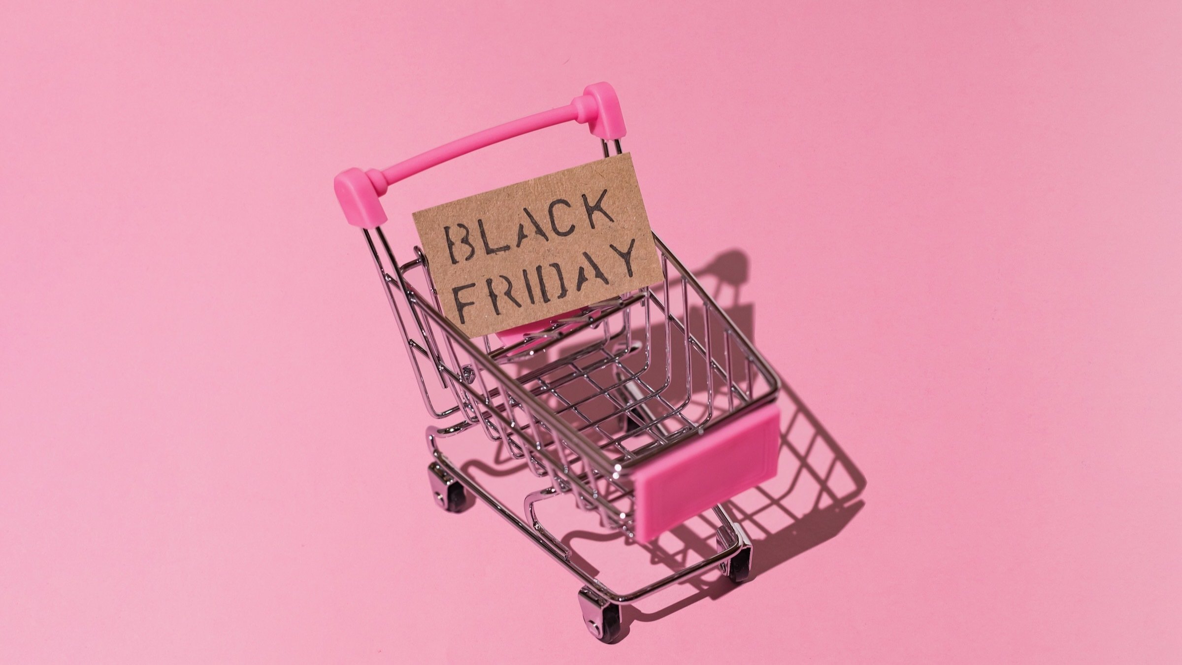 miniature shopping cart with sign that reads 'black friday' on pink background