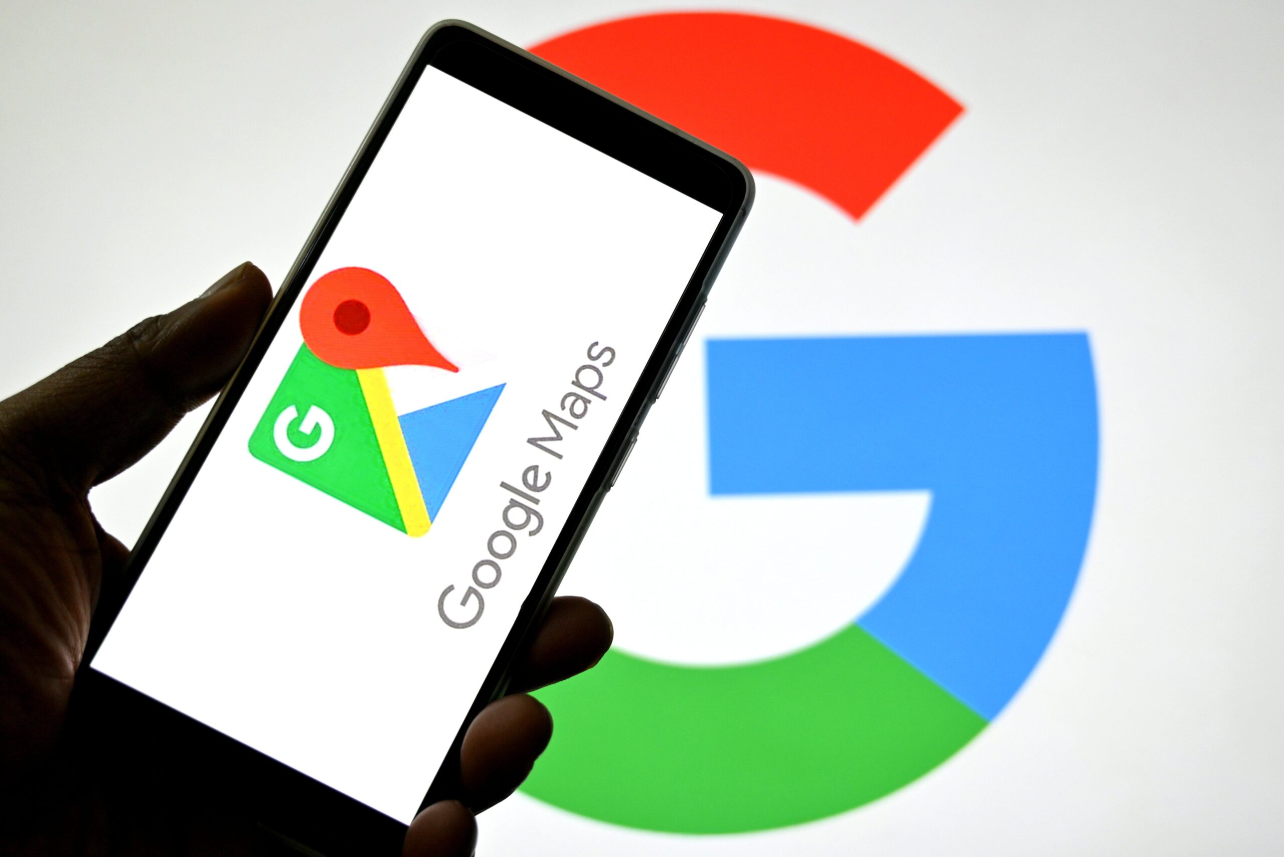 a Google Maps logo is seen displayed on a smartphone with a Google logo in the background