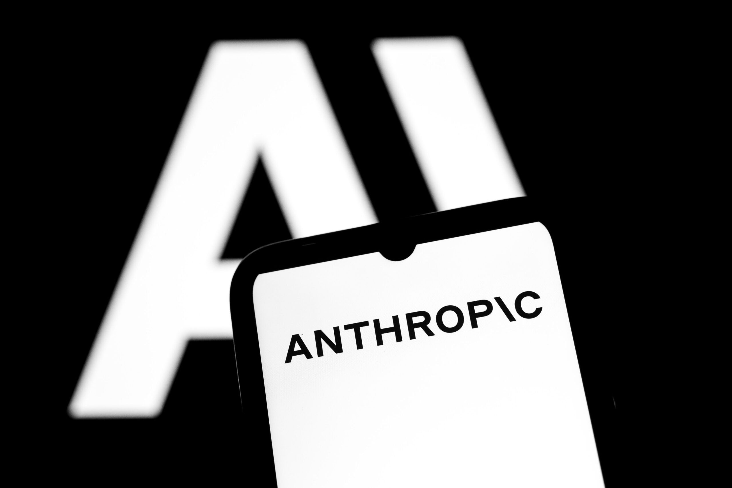 The Anthropic logo appears on a smartphone screen and as the background on a laptop computer screen in this photo illustration in Athens, Greece, on November 12, 2025. Anthropic PBC plans to spend $50 billion to build custom data centers for artificial intelligence work in several US locations, including Texas and New York, as the latest expensive pledge for infrastructure to support the AI boom.