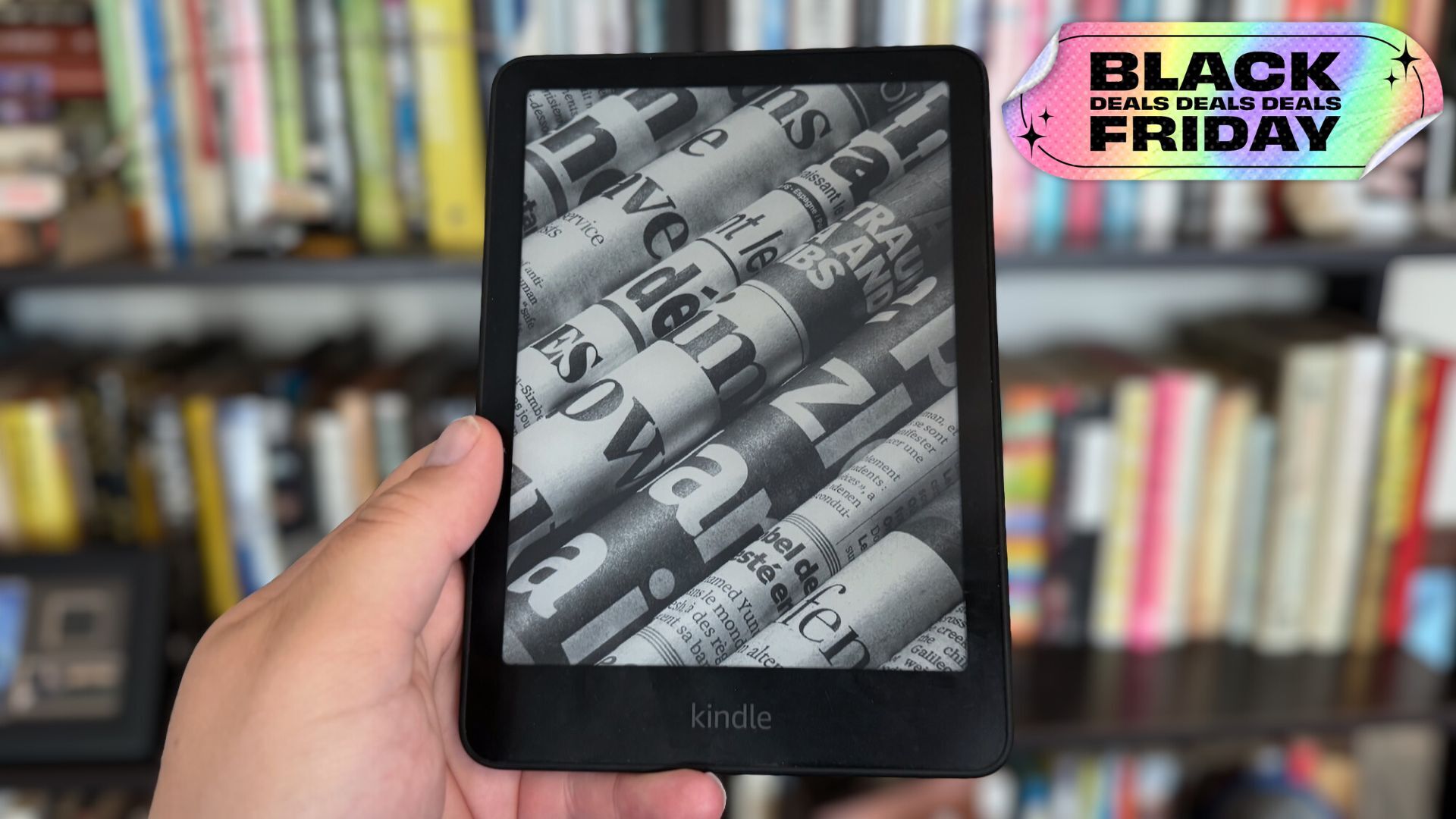 kindle held up in front of bookshelf with sticker that reads 'black friday deals'