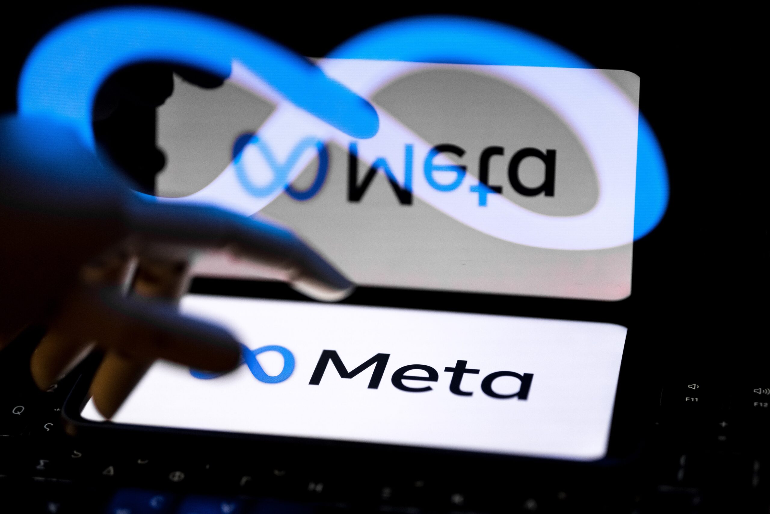 A hand hovers over a screen showing the Meta logo. The image is reflected and distorted.
