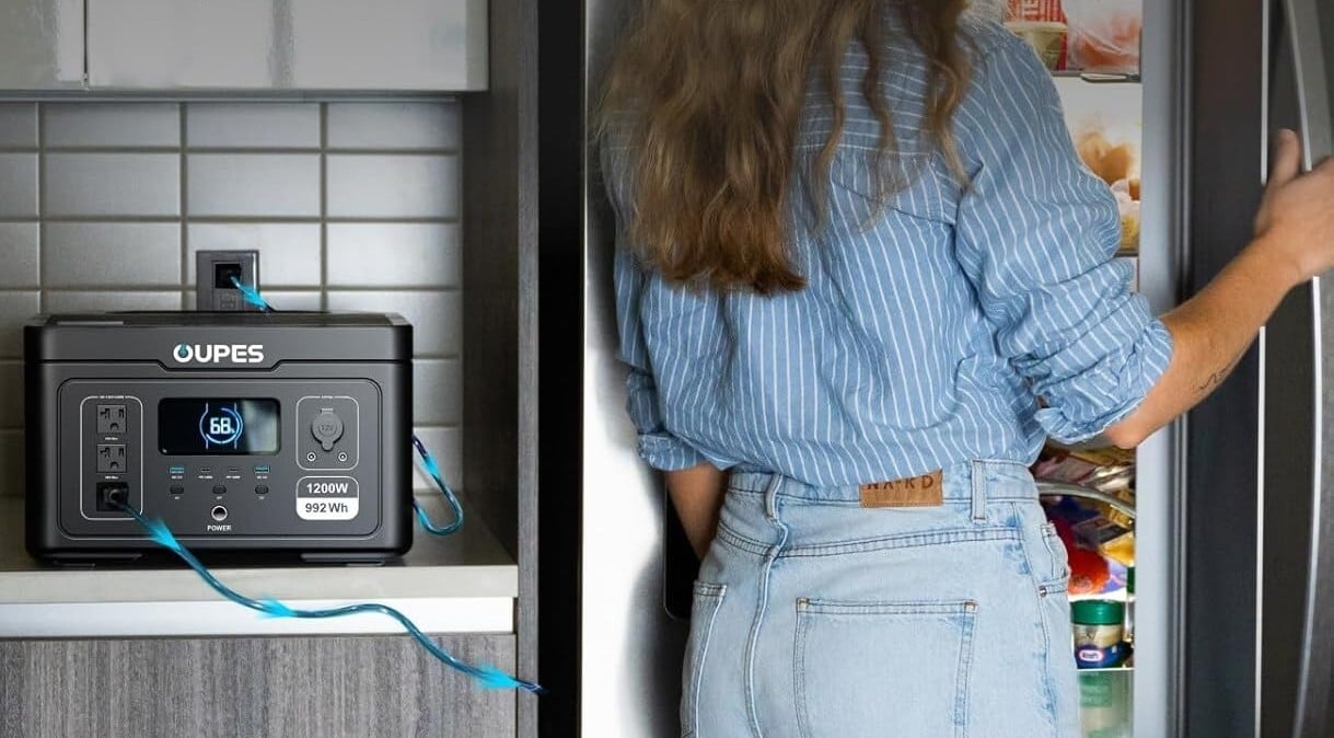 a person uses the oupes exodus 1200 to power the refrigerator. the power station is sitting on the kitchen counter to the left of the refrigerator which a person is standing in front of