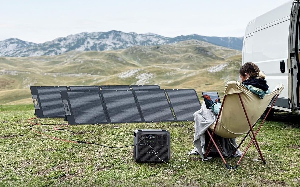 a persons sits in a camp chair next to a van while two solar panels sit in front of her along with the Bluetti elite 200 v2 portable power station
