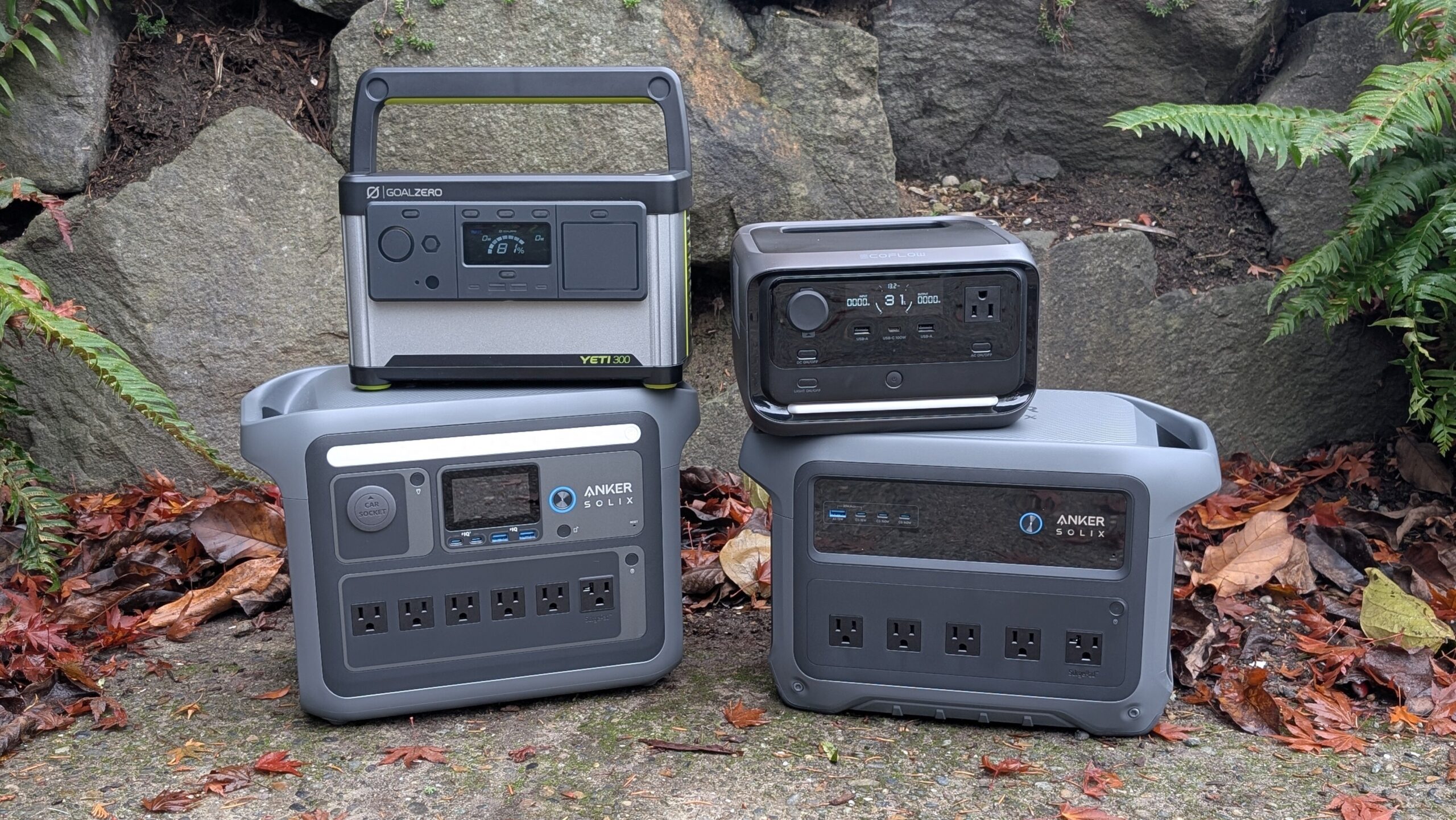 portable power stations from anker, goal zero, and ecoflow arranged together in front of a rockery with fall leaves on the ground