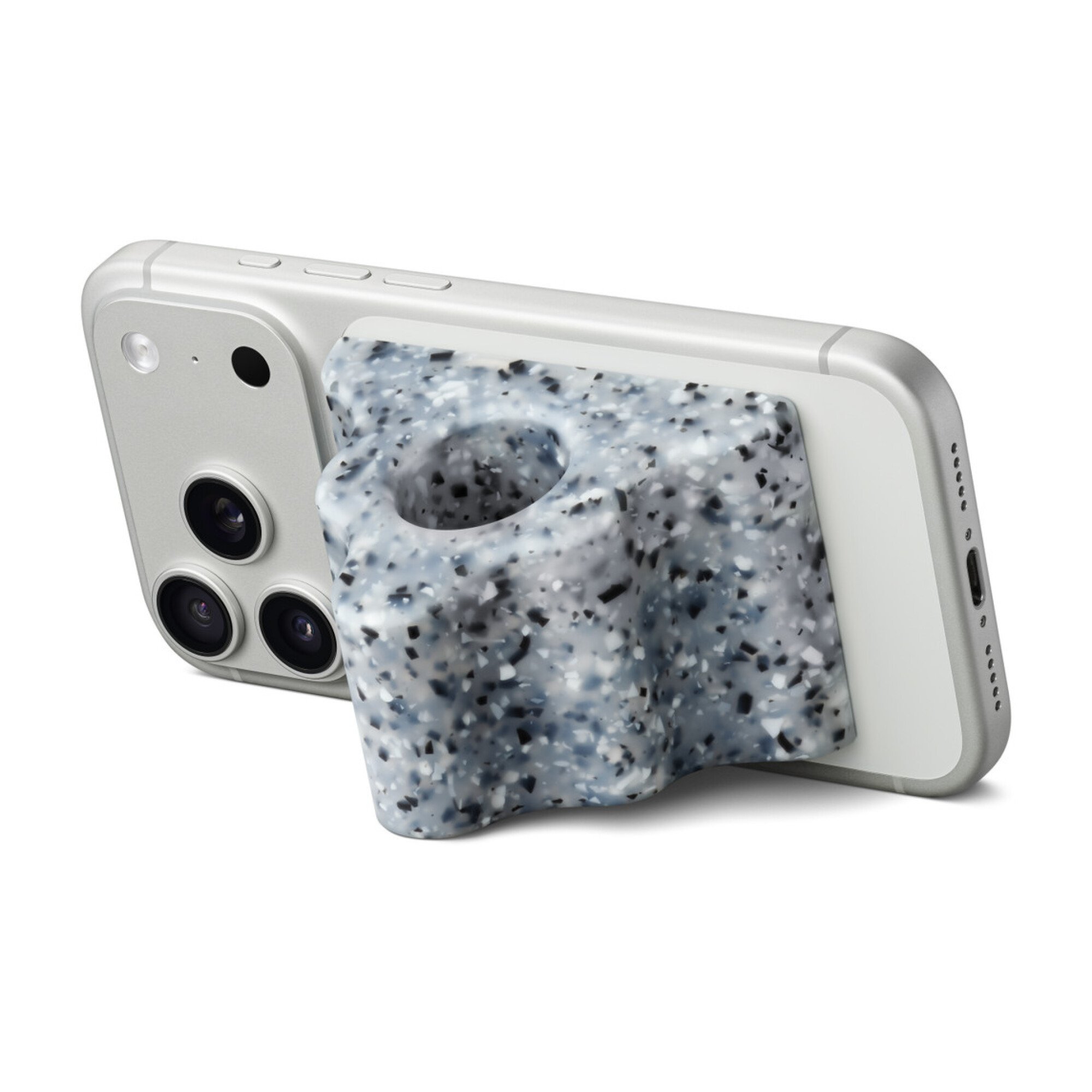 An iPhone rests horizontally with a pyramid shaped accessory magnetized to its back. The accessory is made of multicolor silicon and features ridges along its side, as well as a large hole through the center.