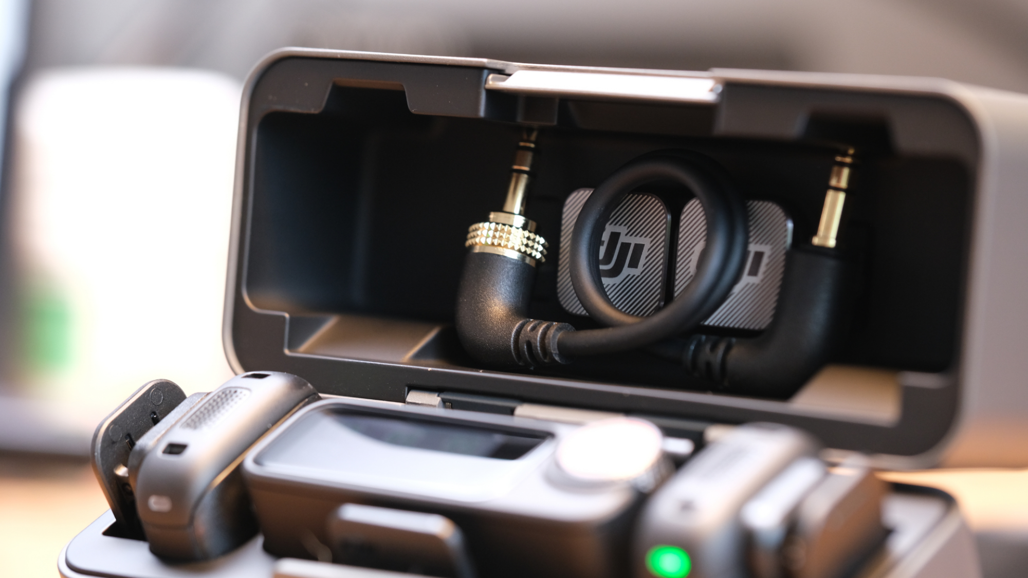 An open charging case for the DJI Mic 3, showing the magnetic clips behind the 3.5mm cable.