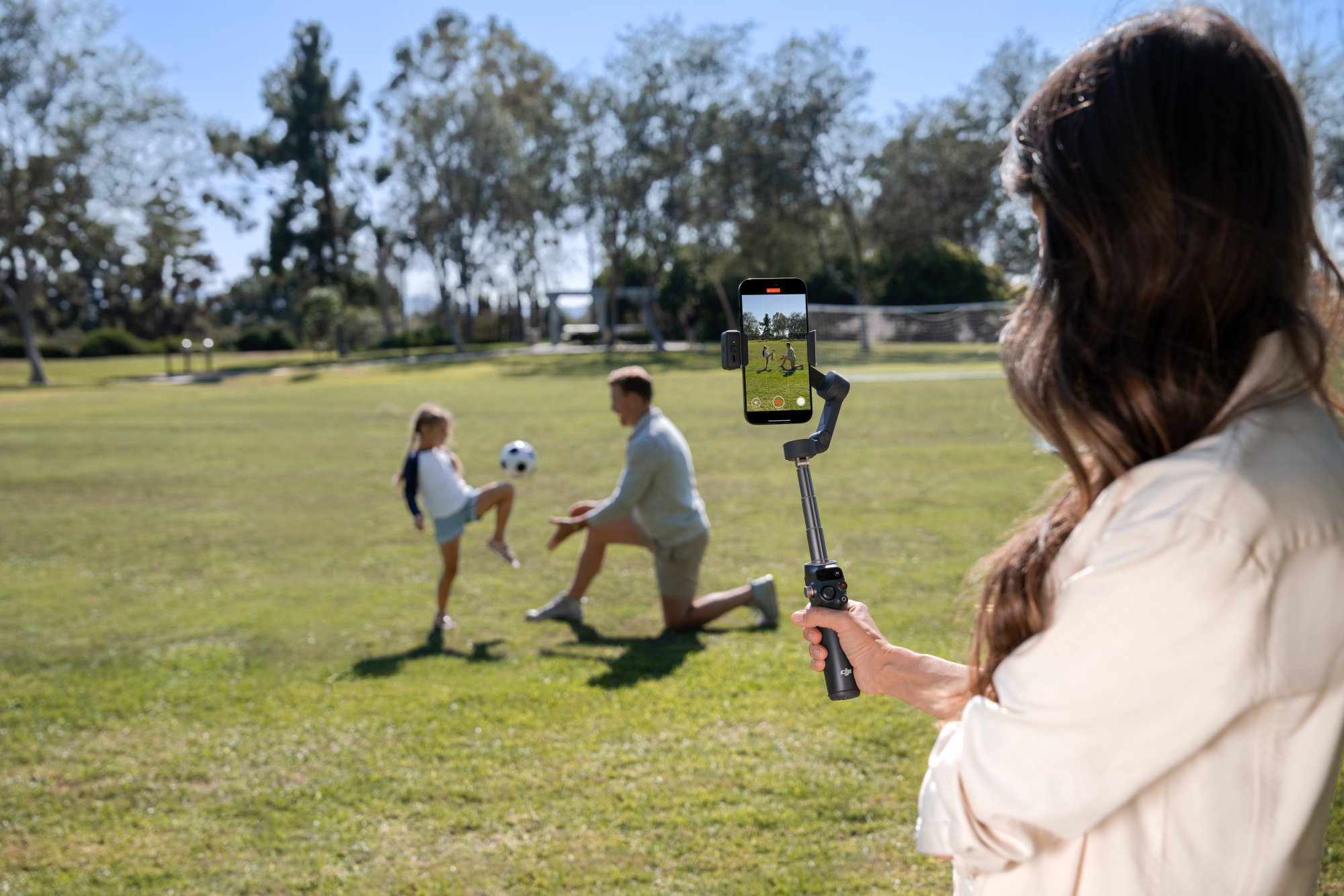 a woman recording a man and a girl playing soccer using the DJI Osmo Mobile 8