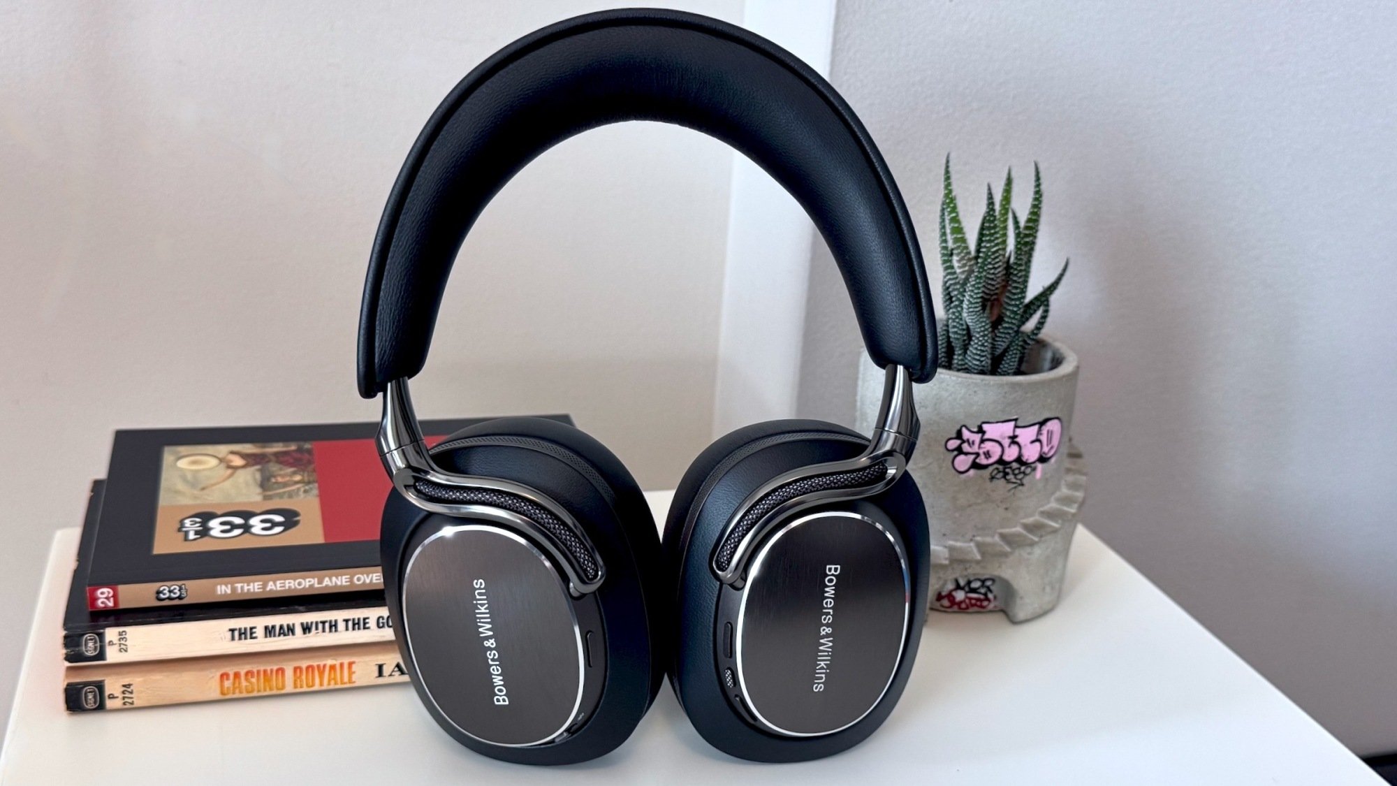 black bowers & wilkins px8 s2 headphones propped on books in front of planter