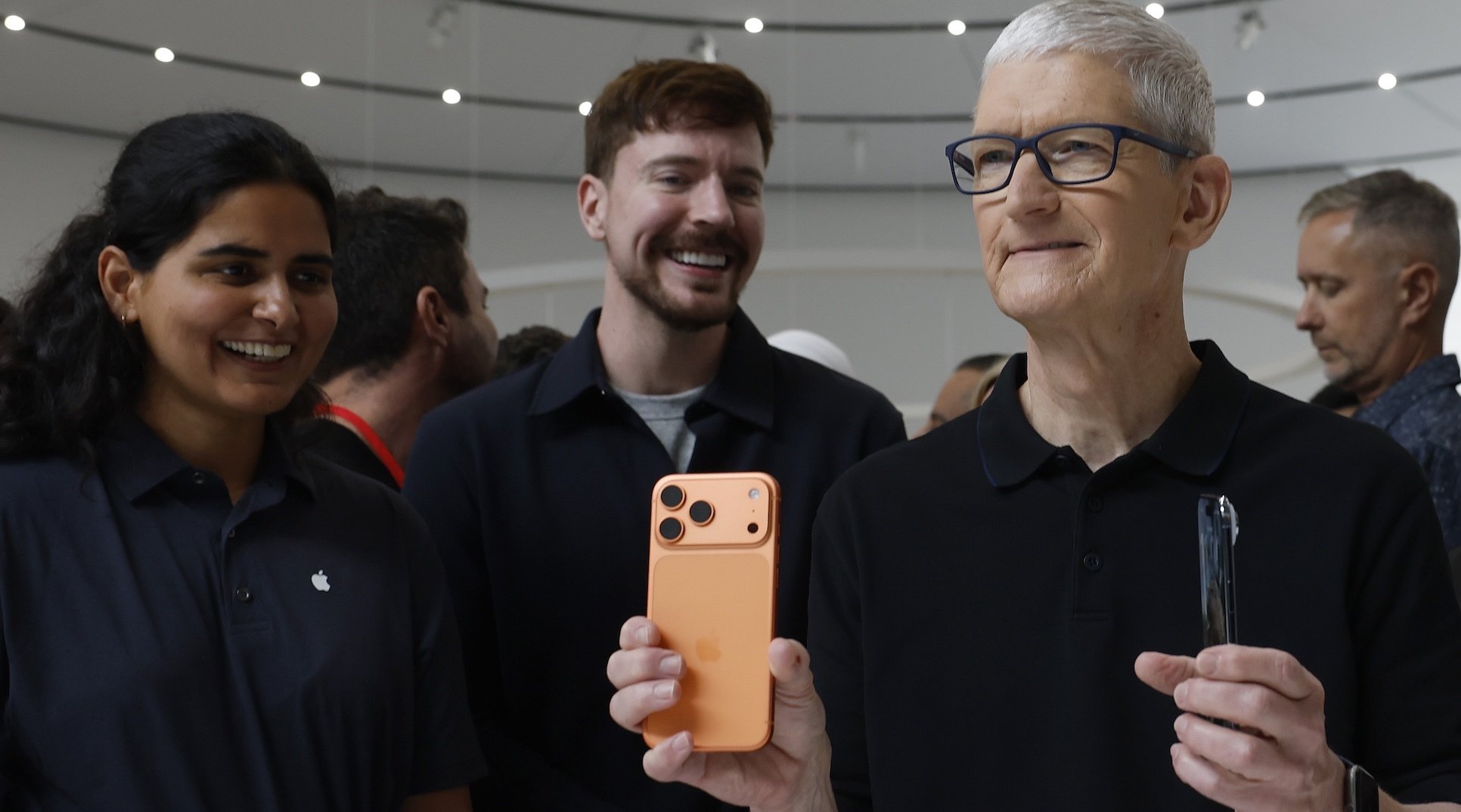 Tim Cook holding iPhone 17s while two young employees smile at him
