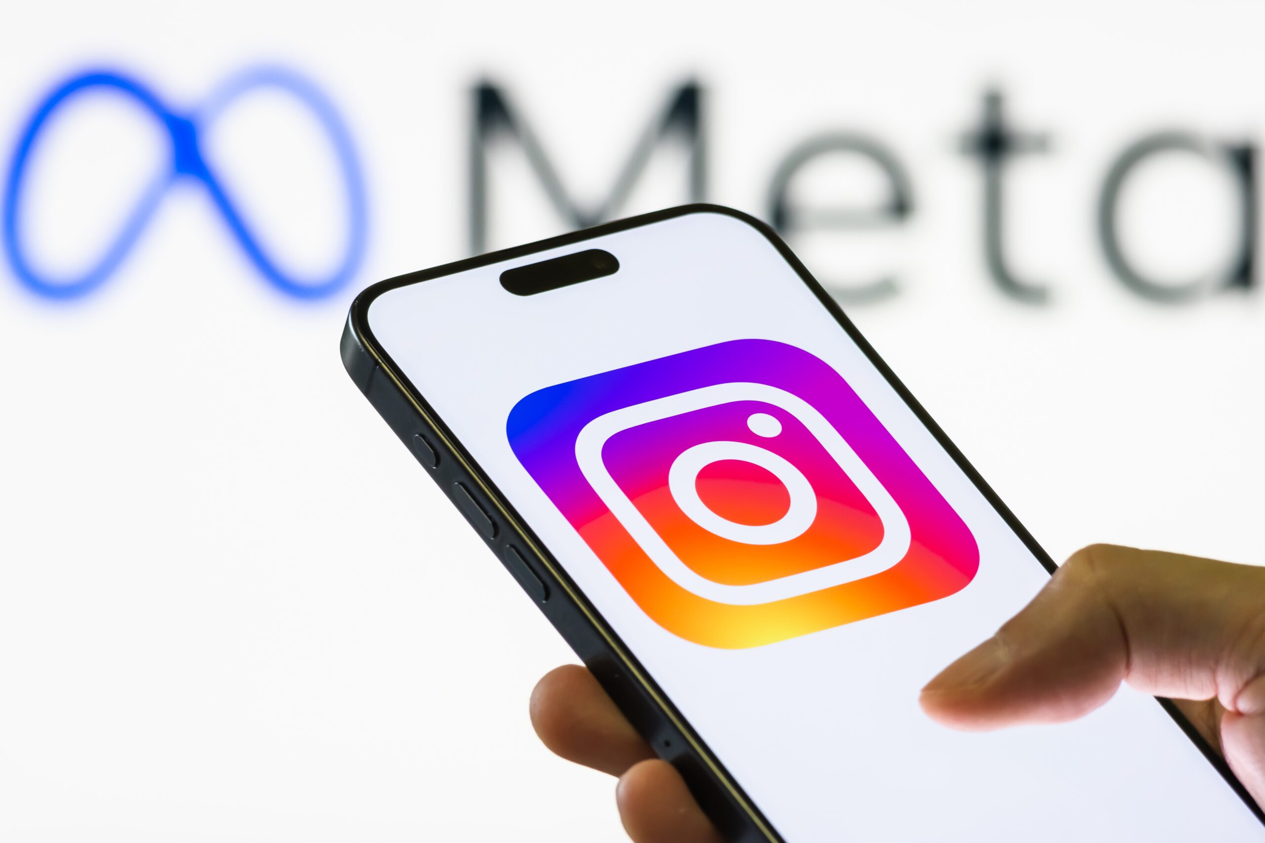 a smartphone held in a hand shows the logo of Instagram, a social media and photo-sharing platform owned by Meta Platforms, with the Meta logo and branding seen in the background