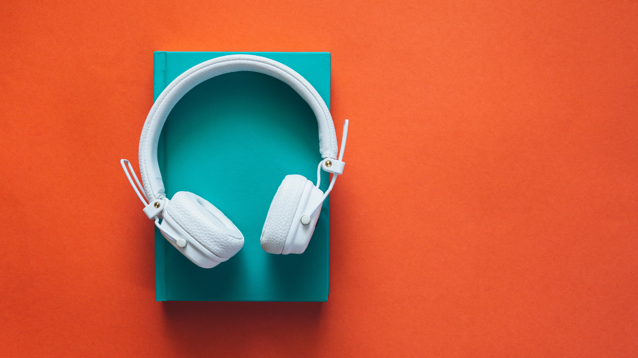 white headphones lying on teal book against orange background