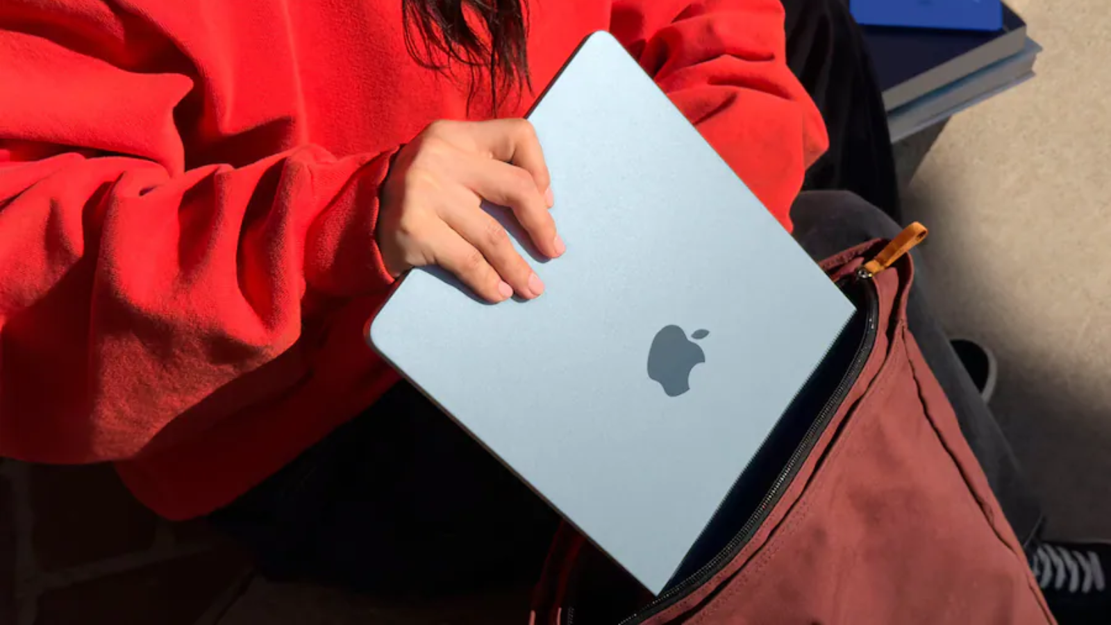a close-up of a girl putting a 13-inch m4 apple macbook air into a backpack
