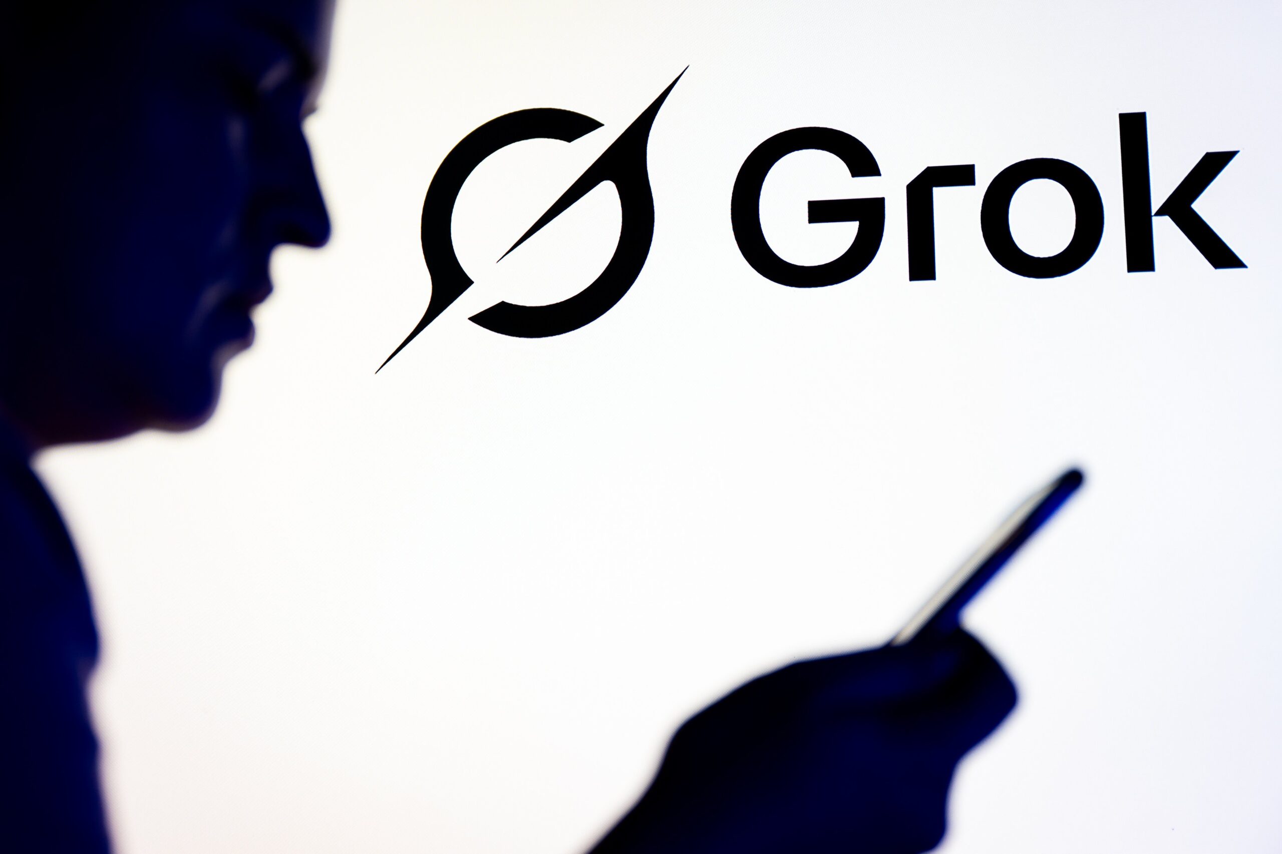 A silhouette of a person reading on a phone in front of the Grok logo.